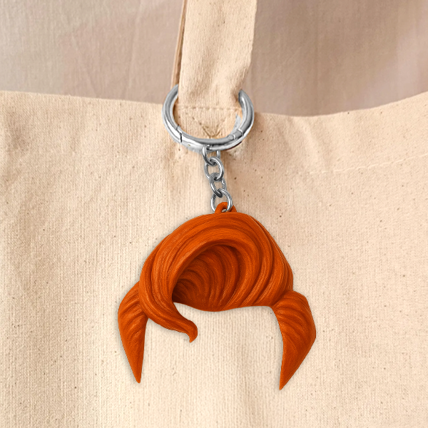 Close-up of a keychain in the shape of stylized orange hair attached to the handle of a cream-colored canvas tote bag with a silver chain and ring.