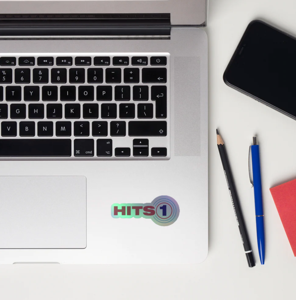 Laptop with 'HITS 1' sticker on a white surface with a phone, pencils, and a notebook.