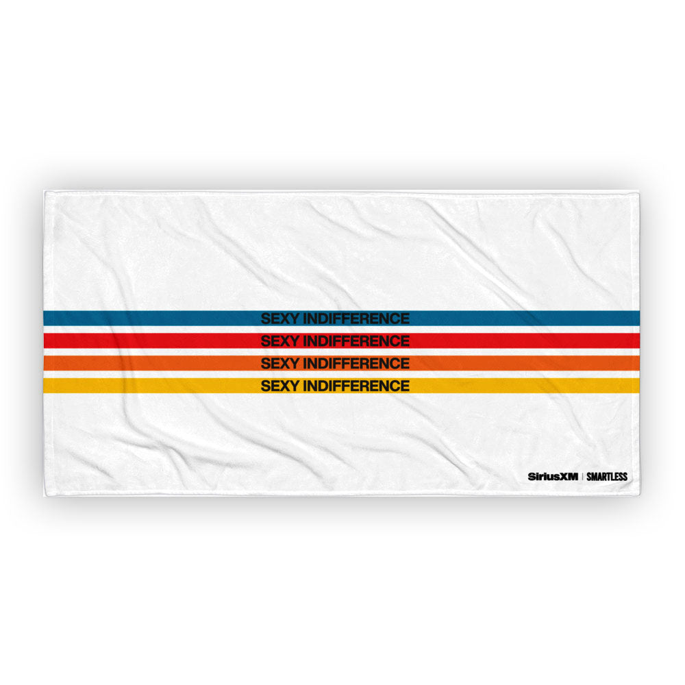A white beach towel featuring four horizontal stripes in blue, red, orange, and yellow, each with the phrase 'SEXY INDIFFERENCE' printed in black. The 'SiriusXM' and 'SMARTLESS' logos are printed in the bottom right corner.