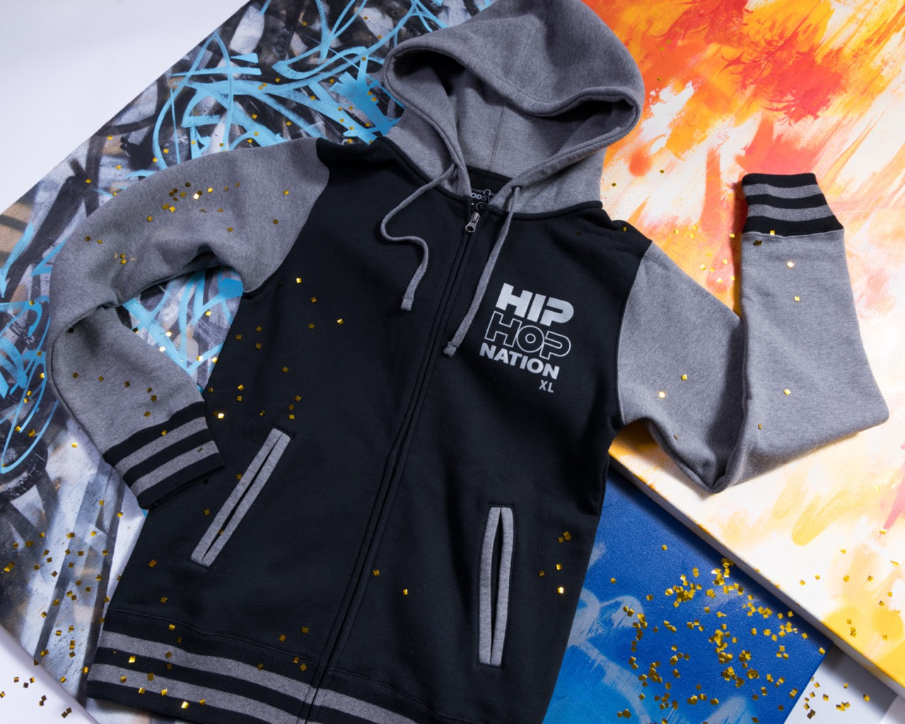 Black and gray hoodie with 'HIP HOP NATION' text, laid on colorful abstract backgrounds with glitter.