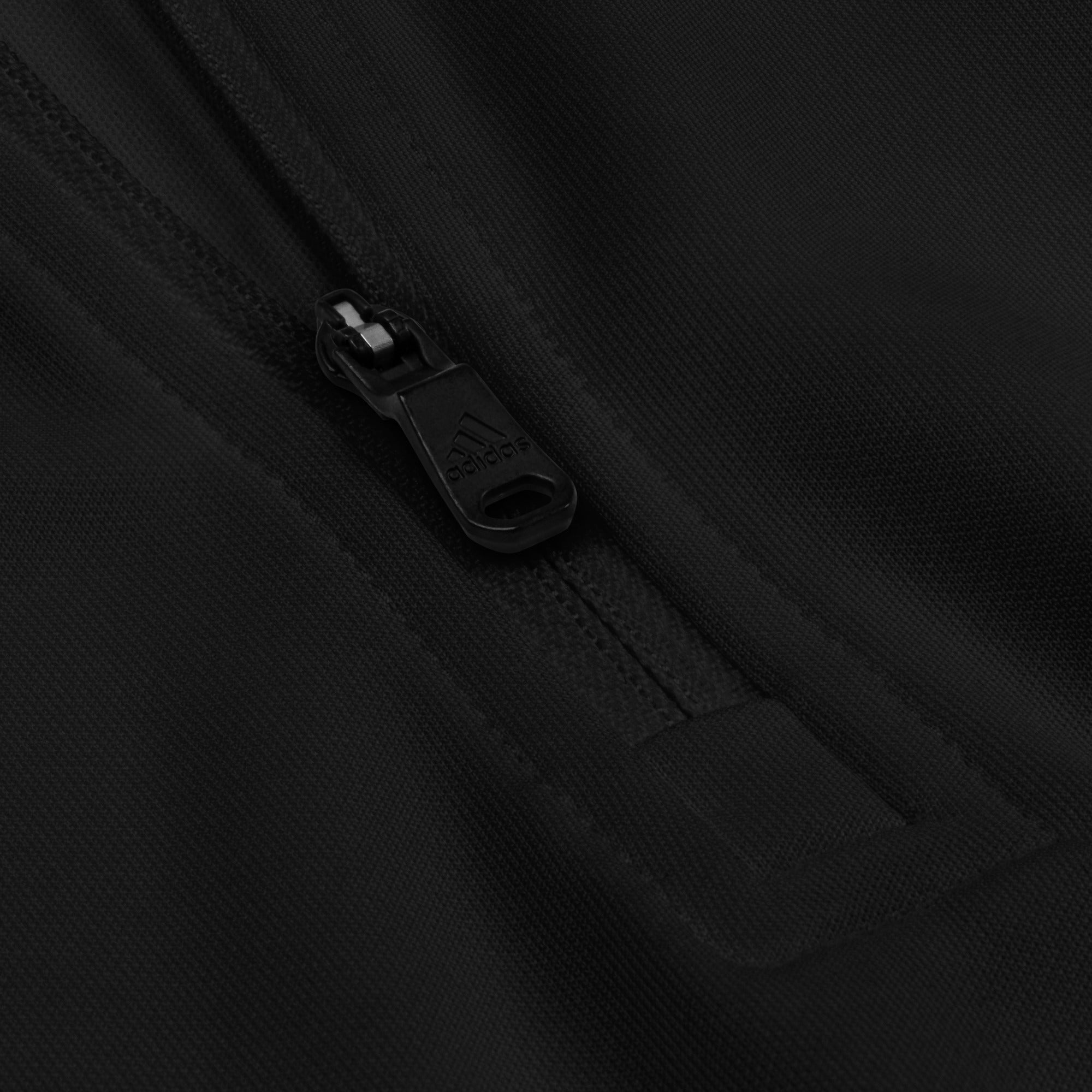 Close-up of a black zipper on fabric, featuring the 'Adidas' logo on the zip pull.