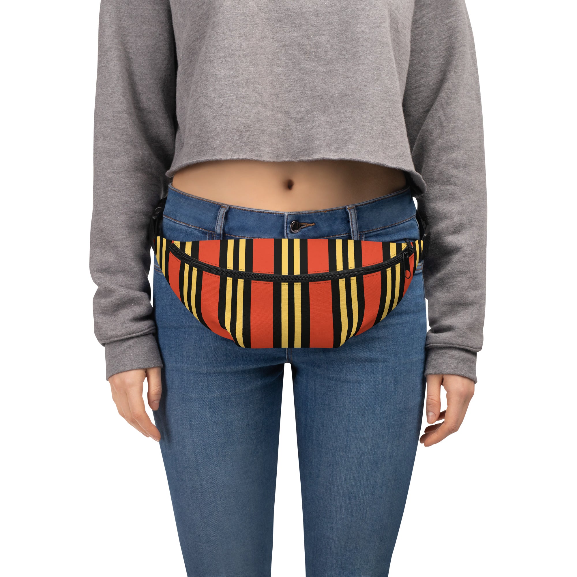 A person wearing a cropped gray sweatshirt and blue jeans with an orange, yellow, and black vertically striped fanny pack fastened at the waist.