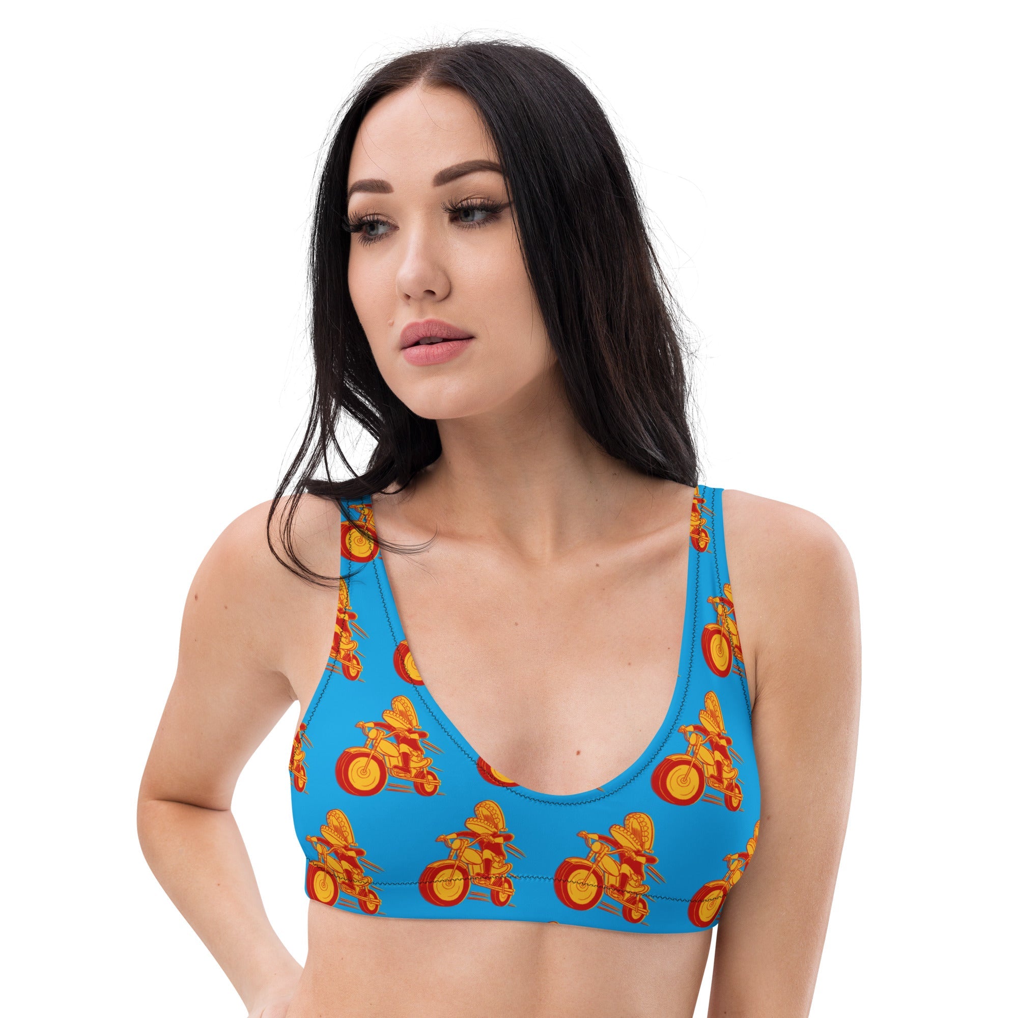 A woman wears a blue scoop-neck bikini top with wide straps and a repeated red and yellow Motormouth motorcycle character pattern, standing against a white background.