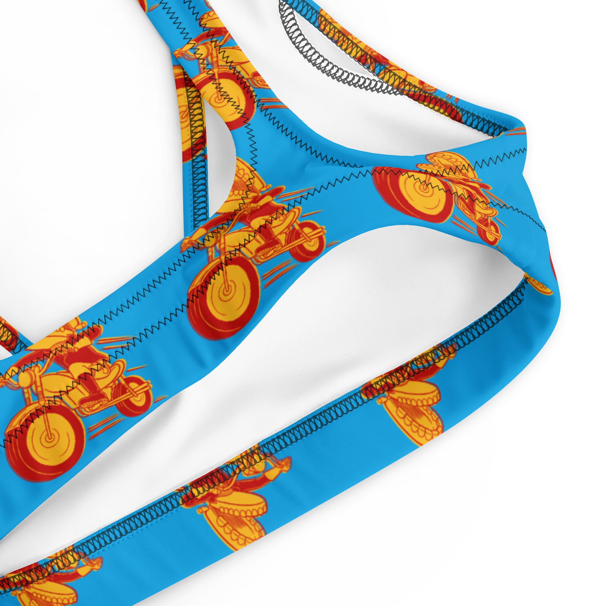 A close-up of the inside edge of a blue bikini top showing zigzag stitching and a portion of the red and yellow motorcycle print on the outer fabric. The white inner lining and elastic construction are visible.