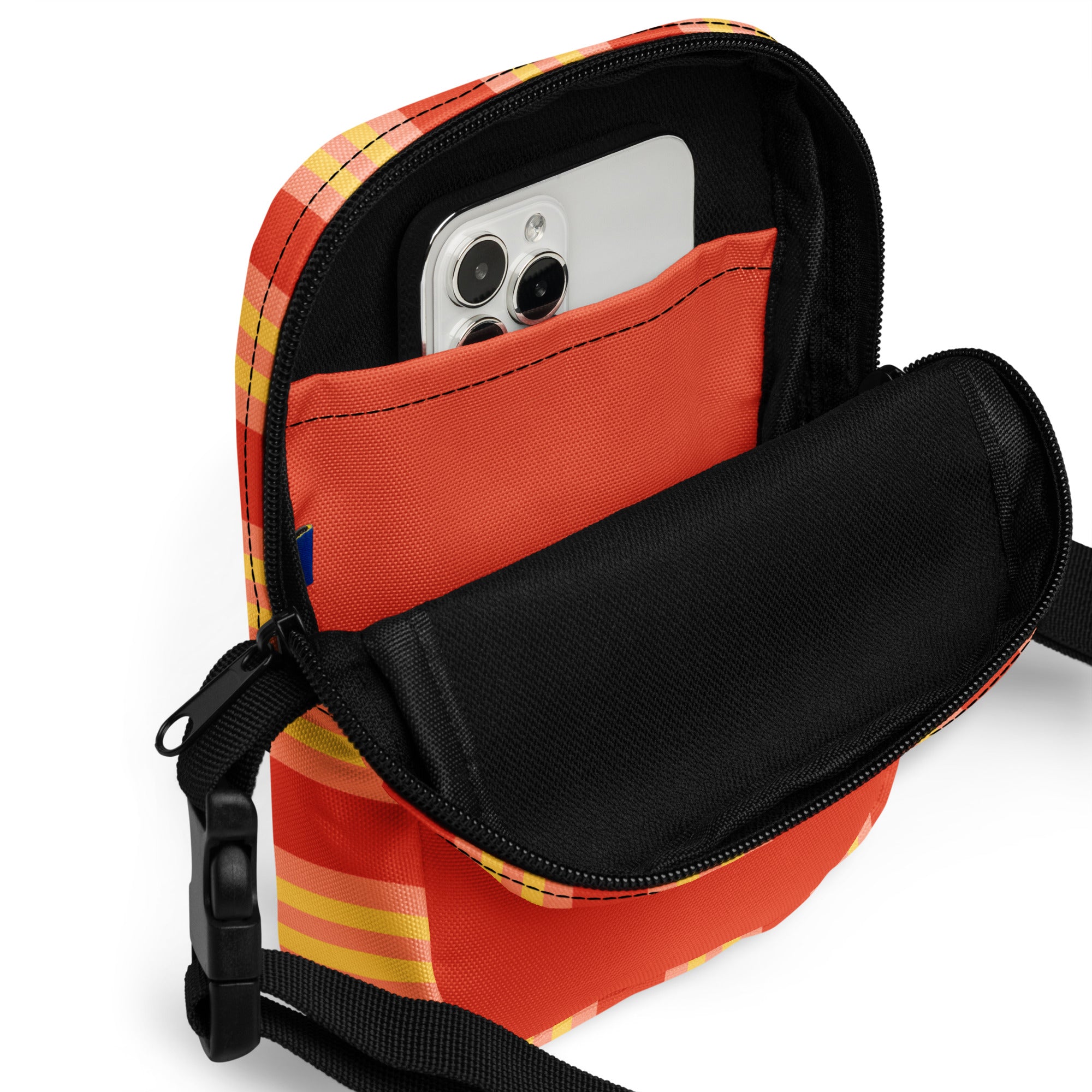 Open view of the crossbody bag showing a zippered main compartment lined in black with an inner orange pocket holding a smartphone. The outer fabric is orange with yellow and light pink stripes.
