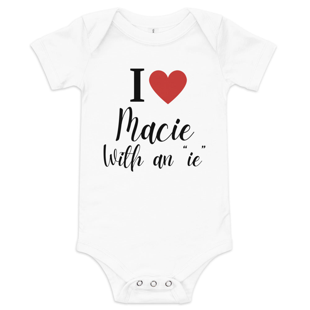 White baby onesie with the text 'I love Macie with an 'ie' in playful script featuring red heart.