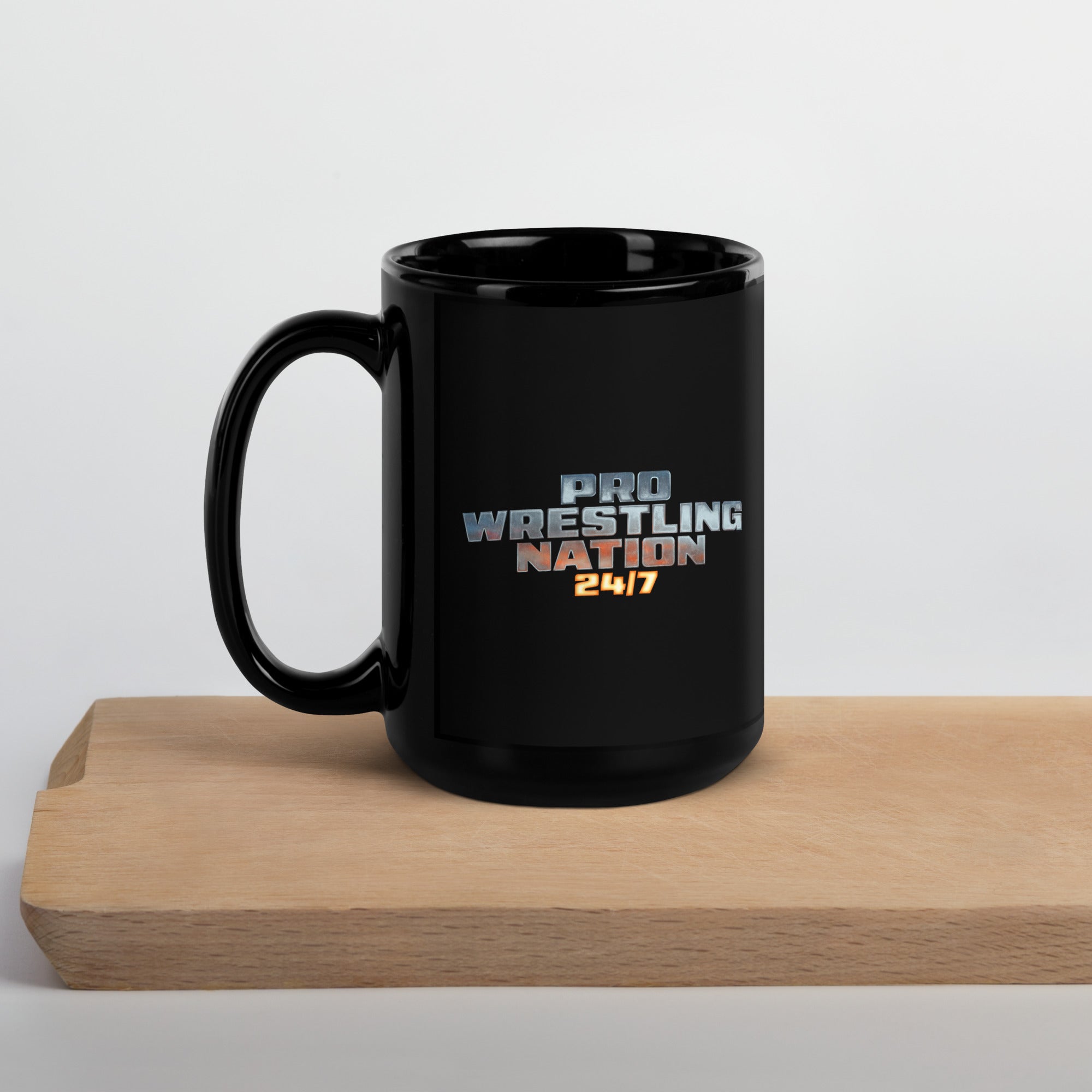 Black 15 oz ceramic mug with 'Pro Wrestling Nation 24/7' logo centered on front, displayed on a light wooden tray against a neutral background.