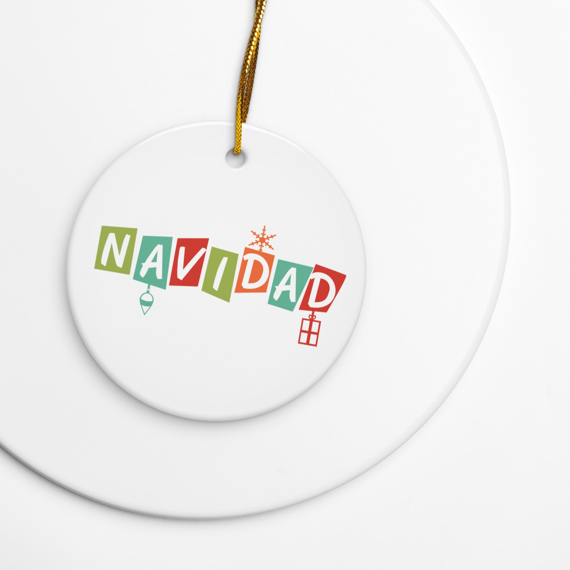 Close-up of a white round ceramic ornament with a gold hanging string, printed with the word ‘NAVIDAD’ in multicolored letters, each letter inside a different colored block, with small festive icons beneath and above.