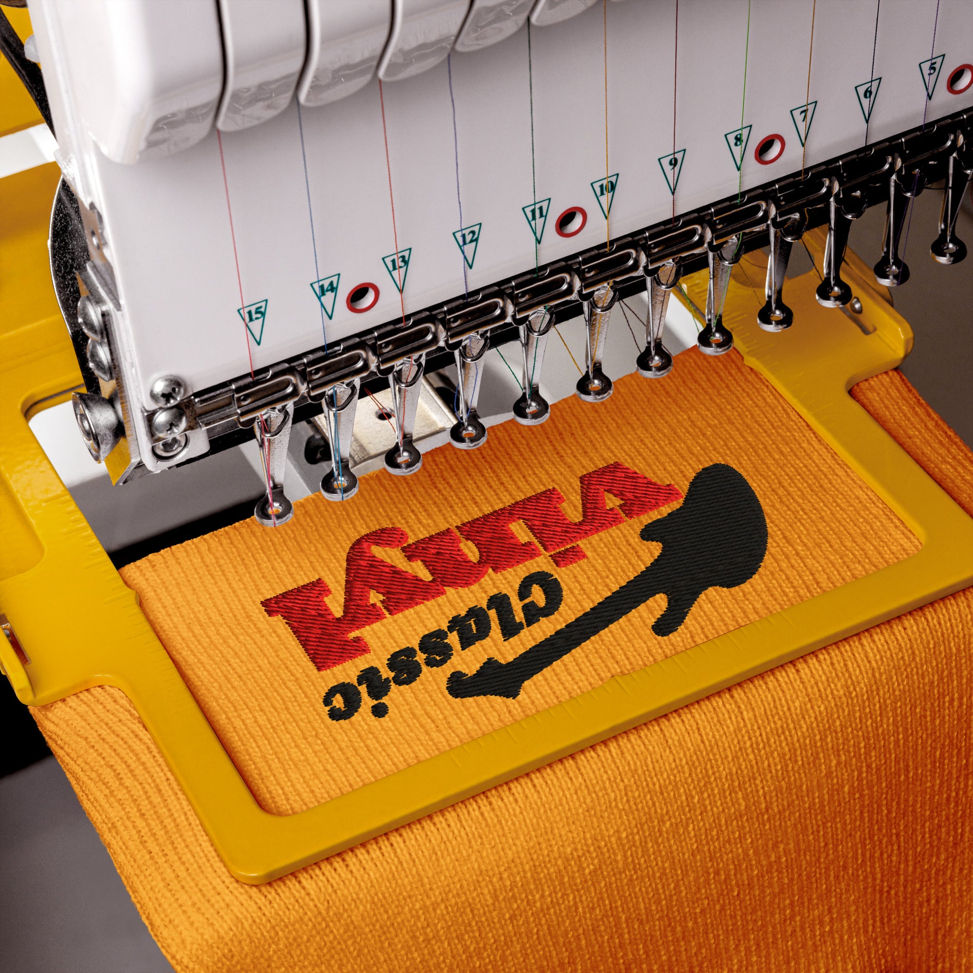 Close-up of an embroidery machine stitching the 'Classic Vinyl' logo in black and red onto a gold knit fabric, showing the threads and needles mid-process.