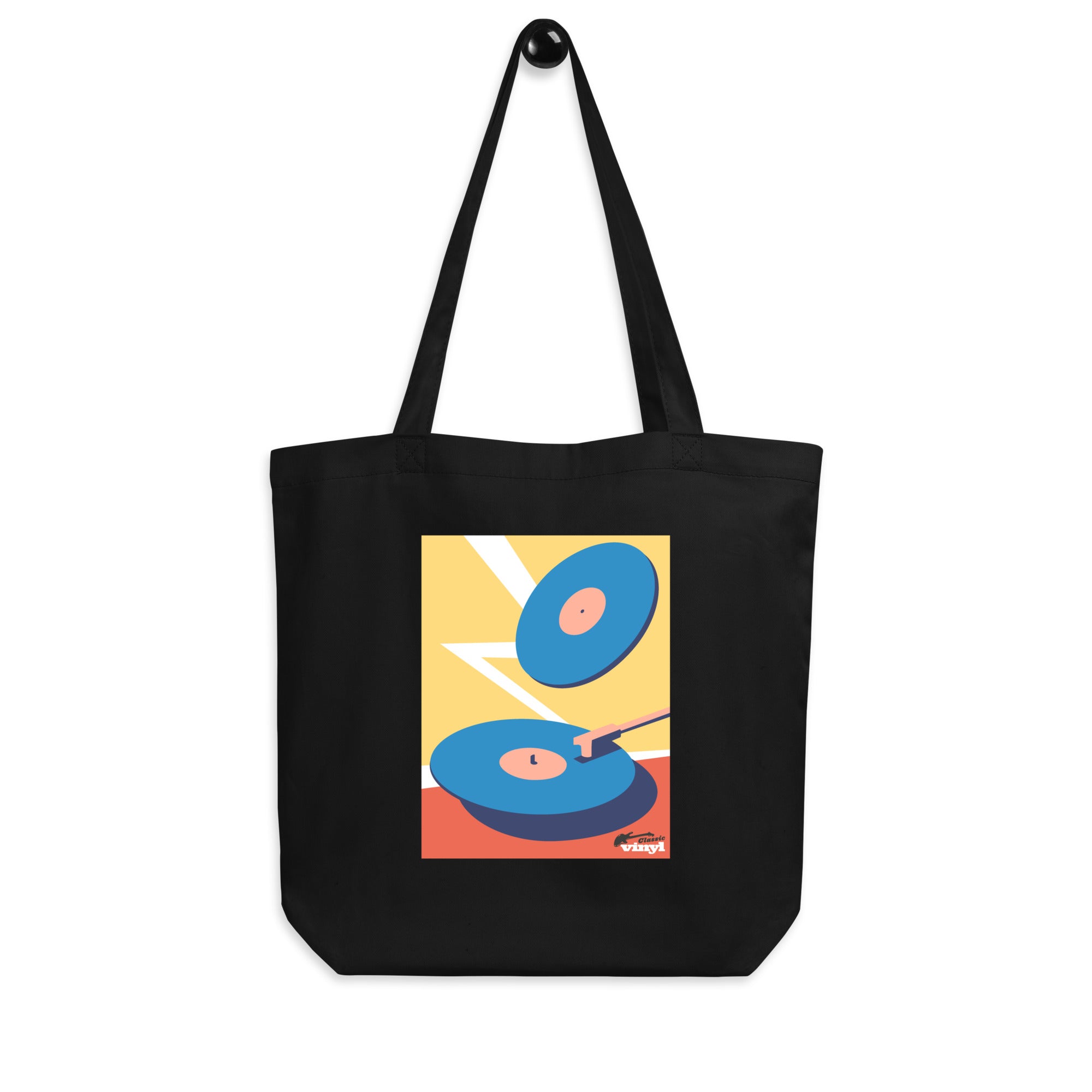 Black tote bag hanging by its handles on a hook, front view. The front displays a bright rectangular design of two blue vinyl records on a red and yellow background with a white zigzag lightning shape, plus the 'Classic vinyl' logo printed in black and red near the lower right corner.