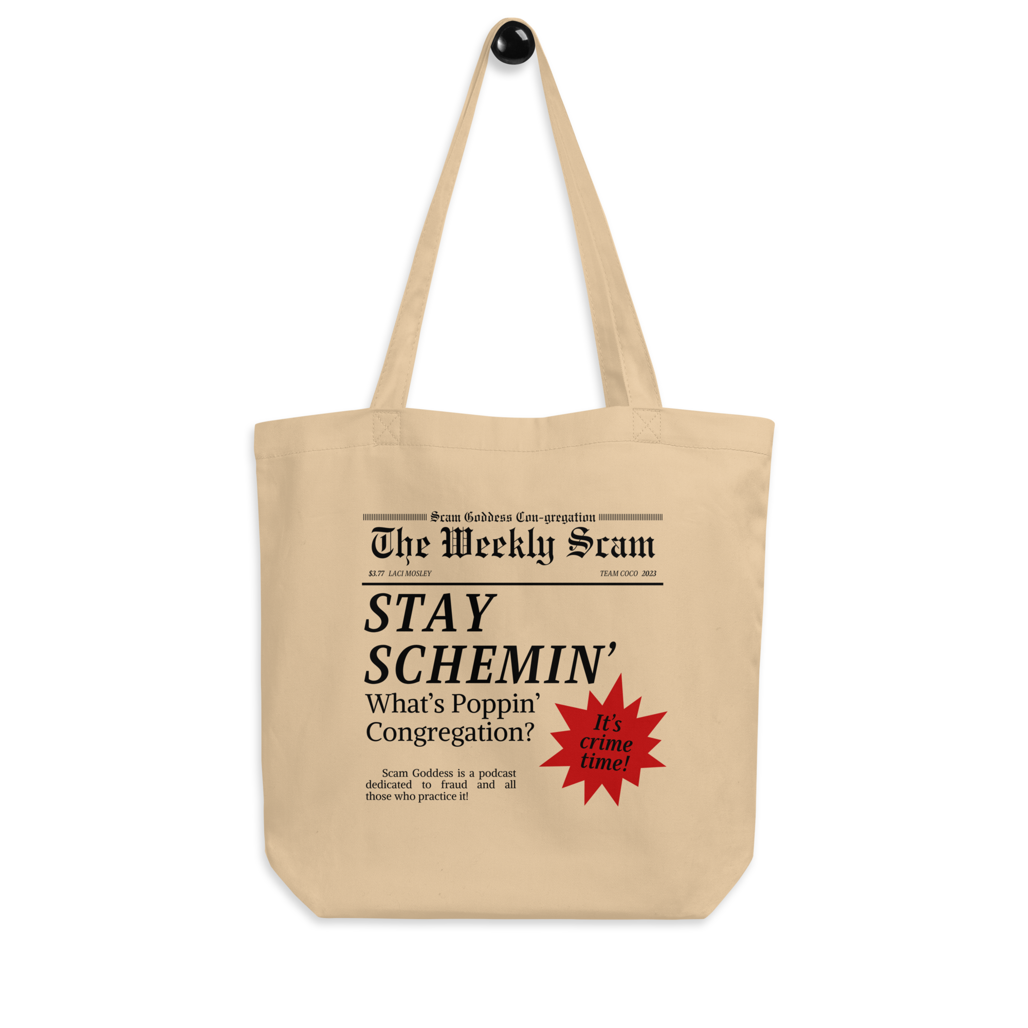 Cream colored tote bag with newspaper-style design featuring the phrase 'STAY SCHEMIN' and 'Scam Goddess' text featuring red sunburst graphic. Bag is on a black background.