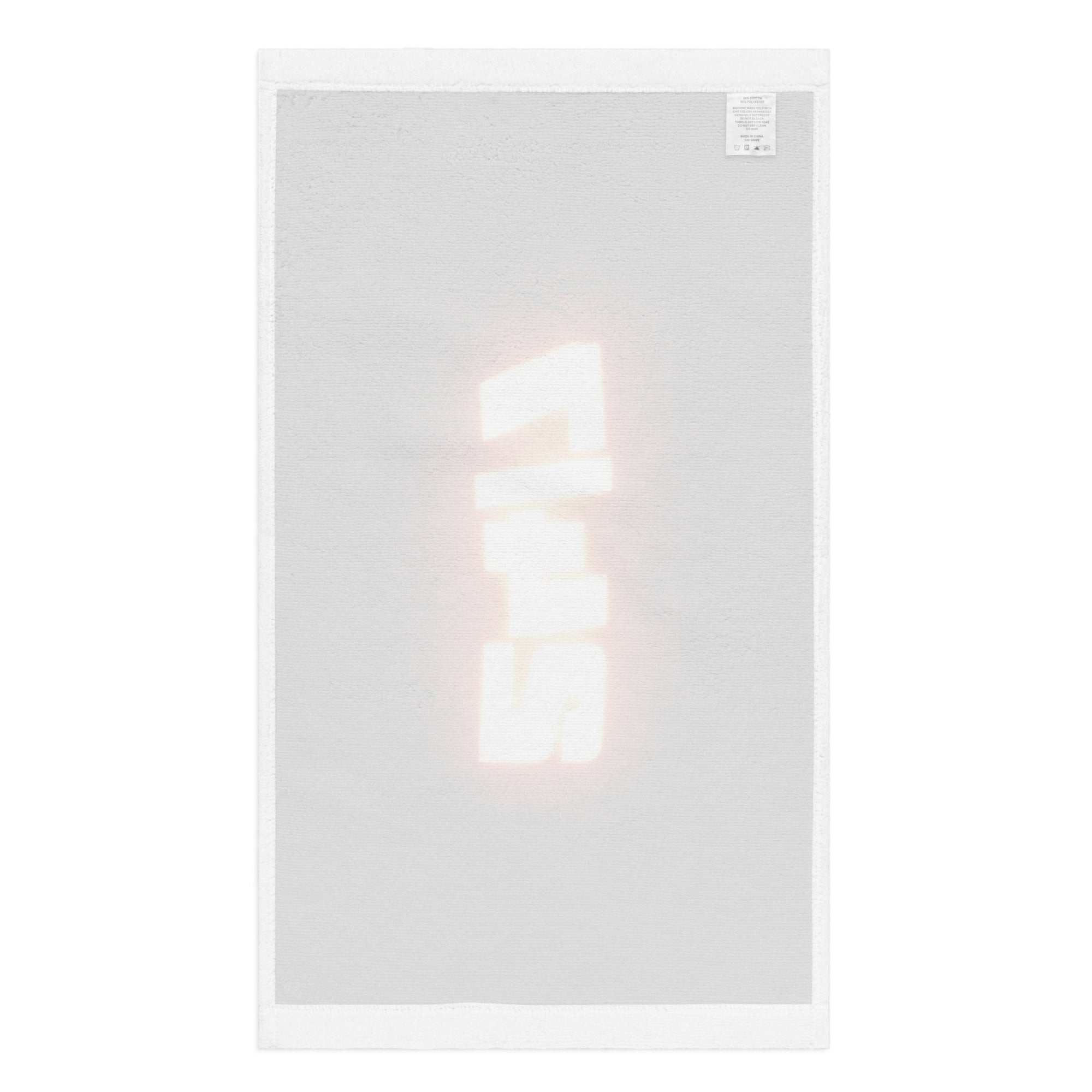 Back view of a white rally towel with a faint reverse print of glowing '24/7' text barely visible through the fabric, shown flat with visible care label.