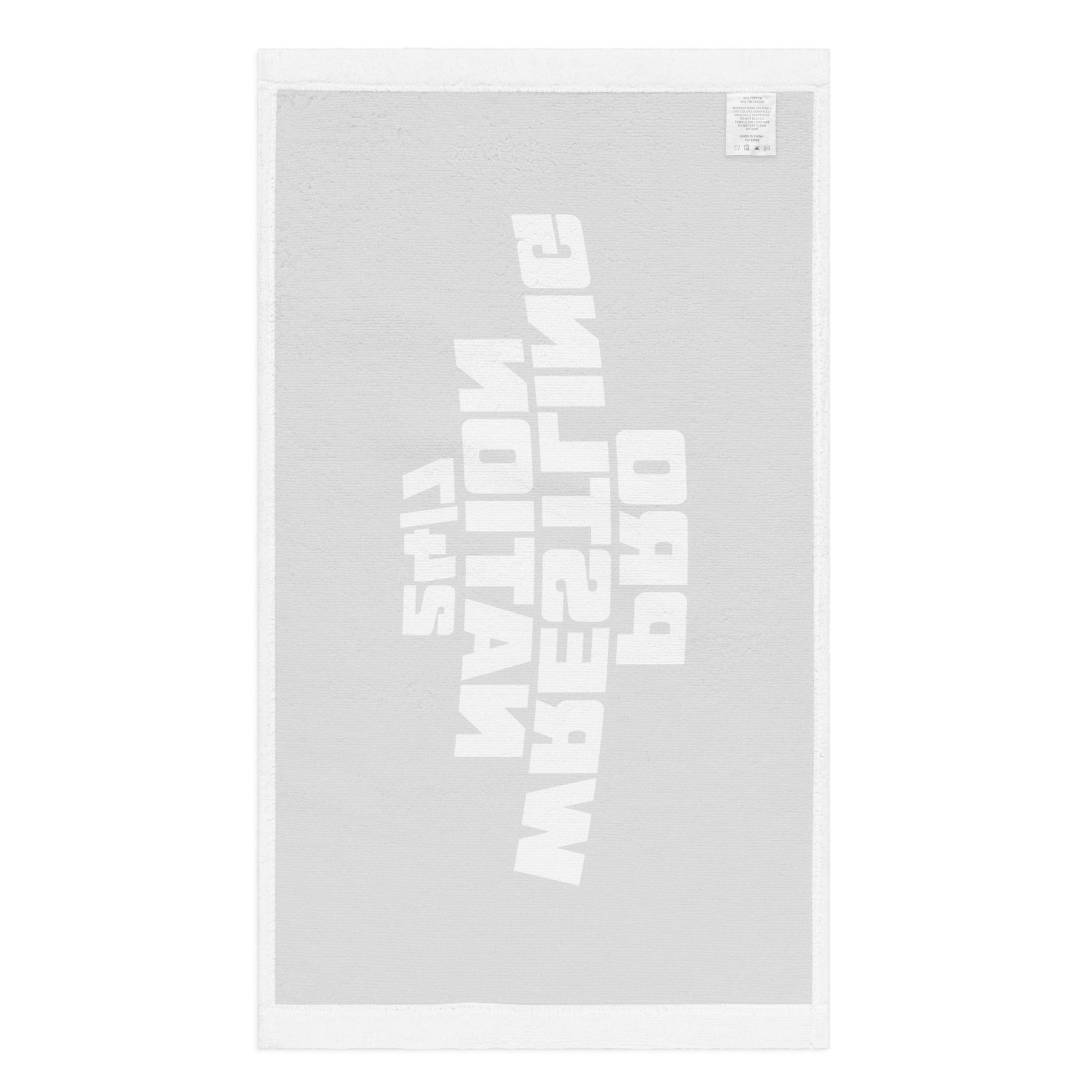 Flat lay of the reverse side of a white rally towel, showing the faint mirrored imprint of the design from the front, with a visible woven care label stitched into the top right corner.