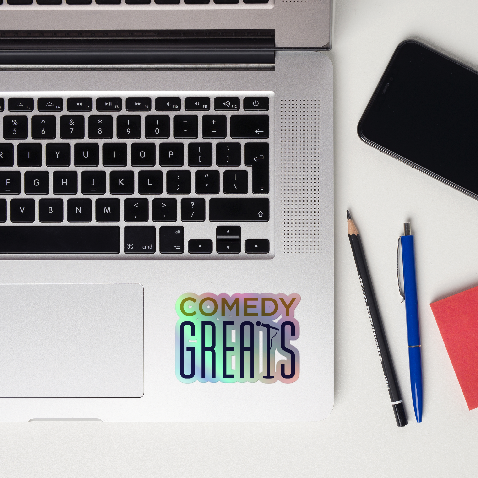 A laptop keyboard displaying a colorful 'COMEDY GREATS' holographic sticker.