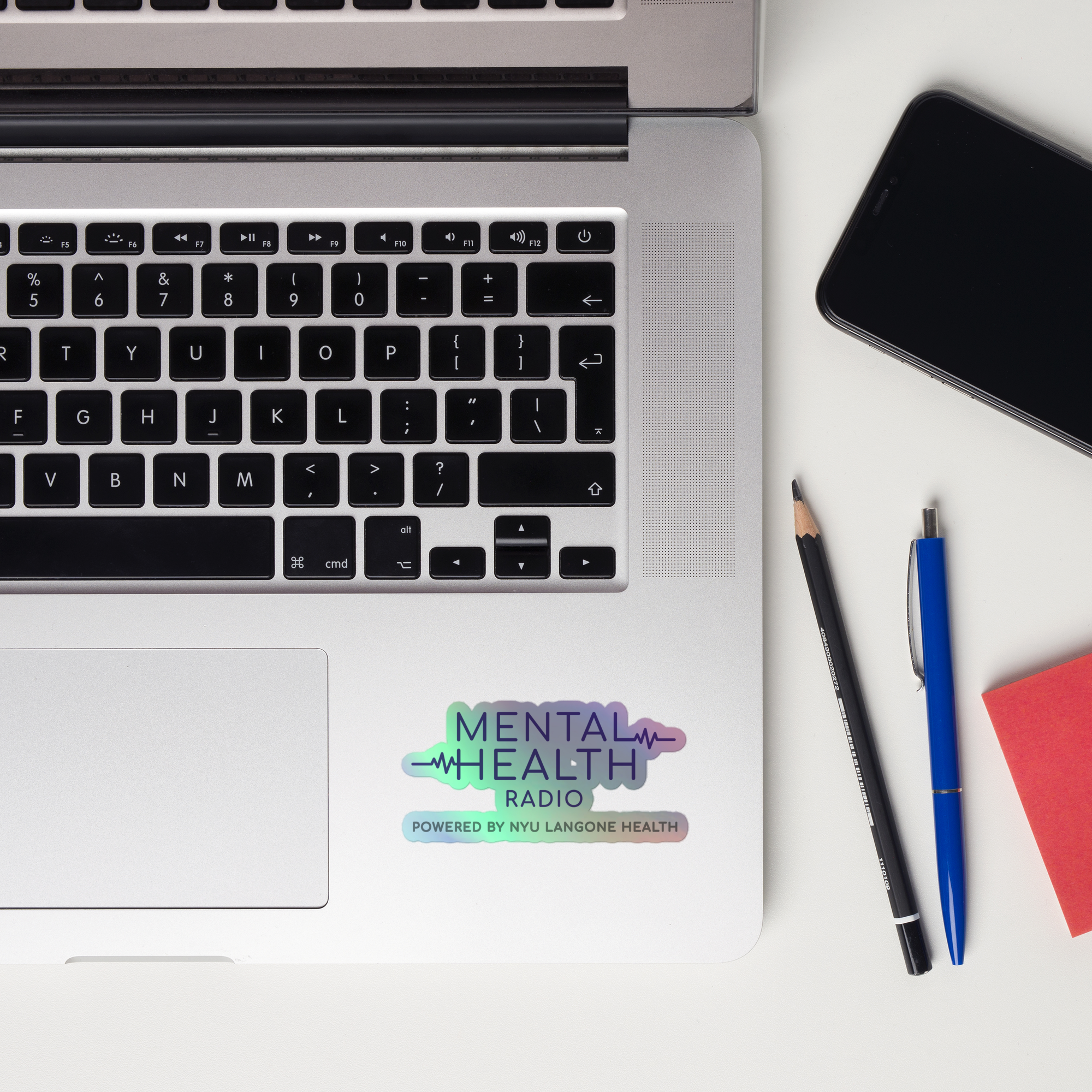 A laptop keyboard displaying a colorful holographic sticker of the 'Mental Health Radio powered by NYU Langone Health' logo.