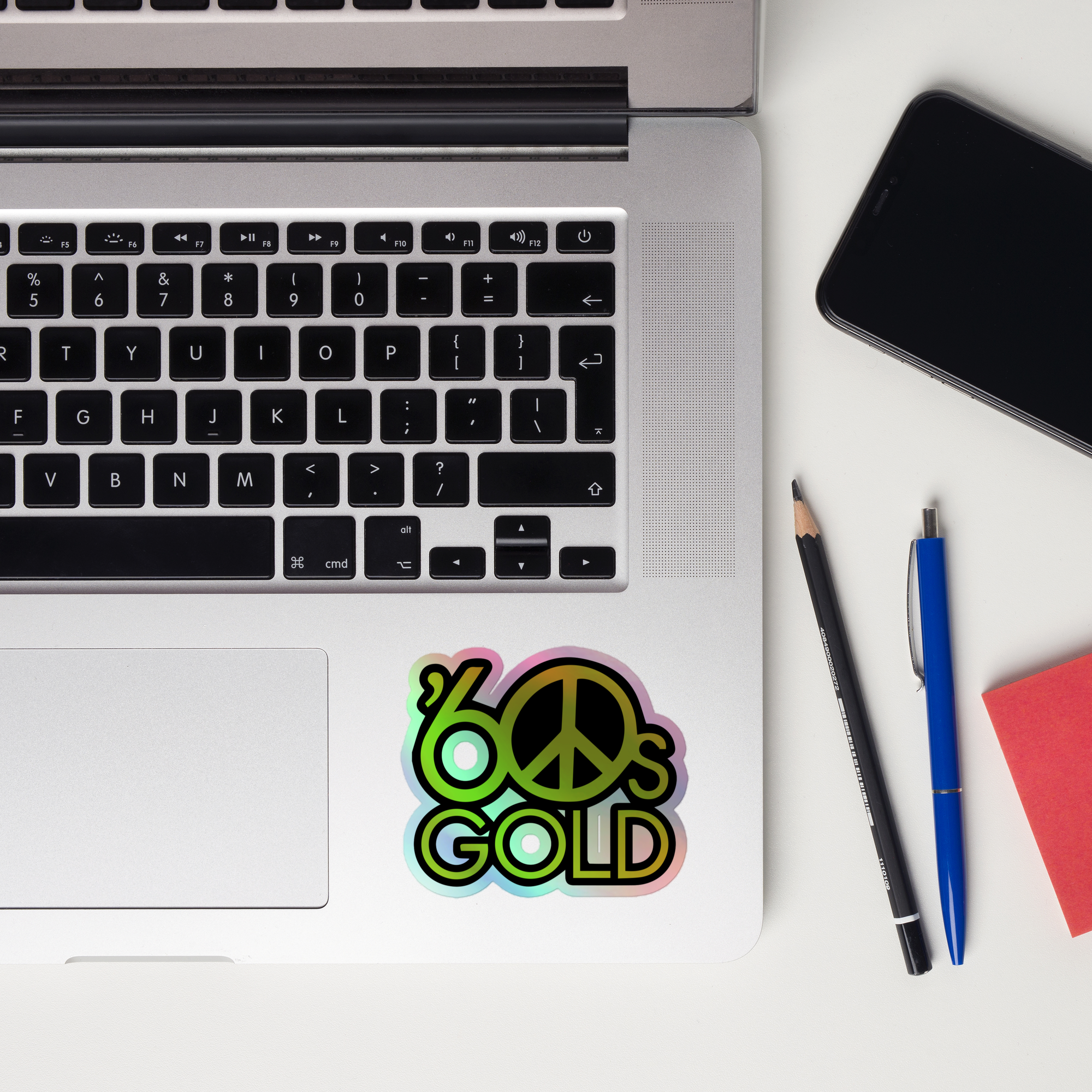 Laptop keyboard displaying colorful '60s Gold' holographic sticker, featuring a peace symbol.