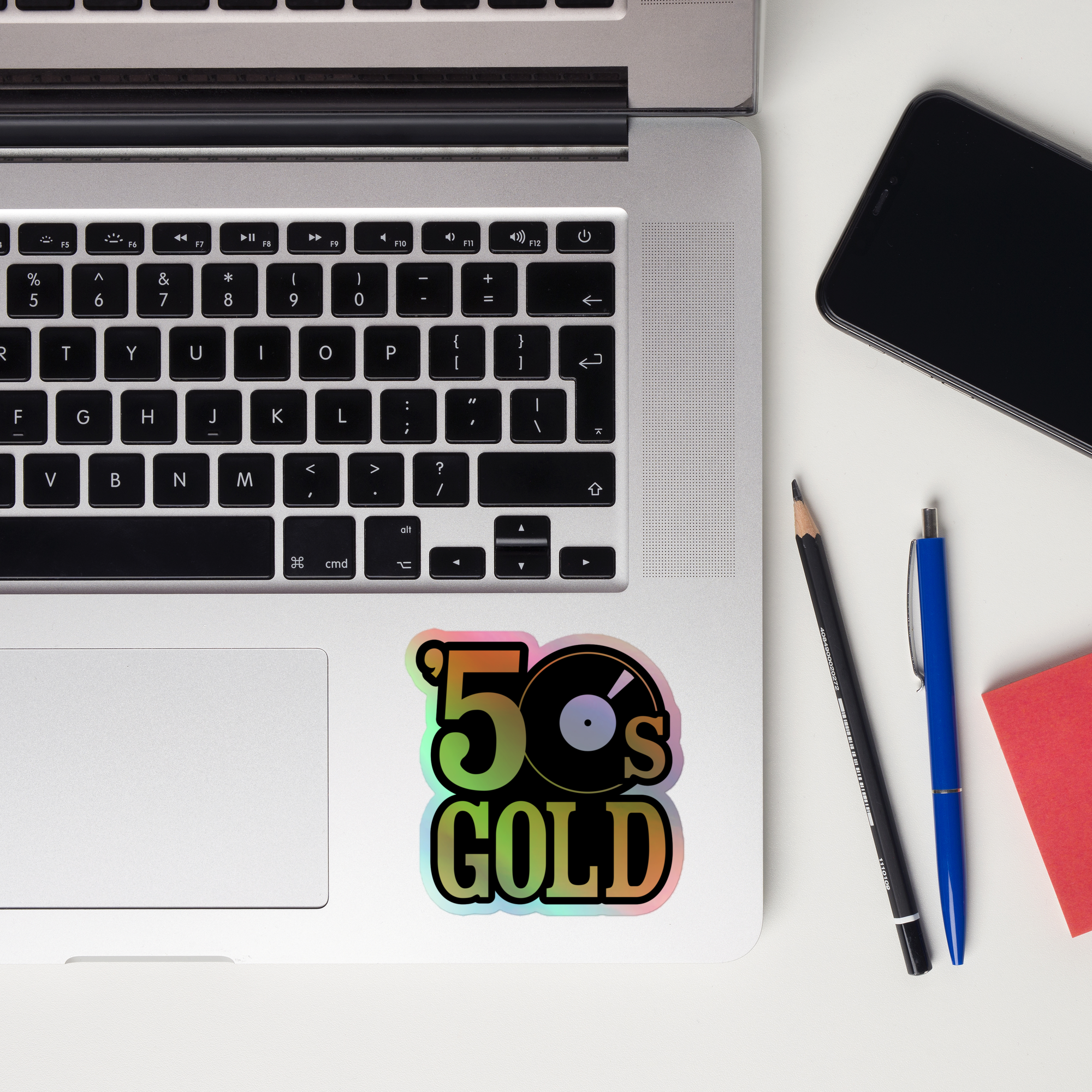 A laptop keyboard displaying a colorful '50s GOLD' holographic sticker.