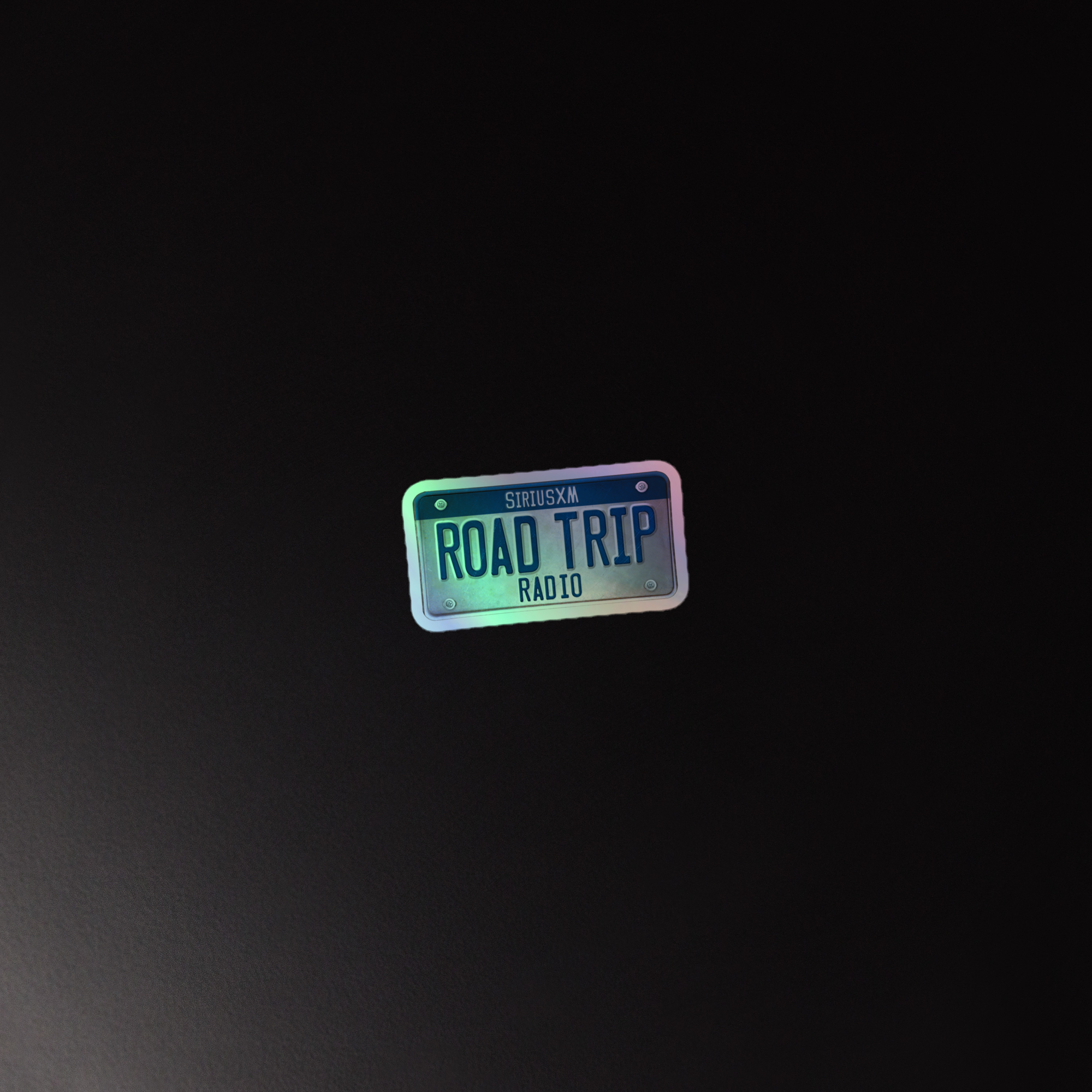 A holographic sticker of the 'SiriusXM ROAD TRIP RADIO' logo that resembles a license plate, on a black background.