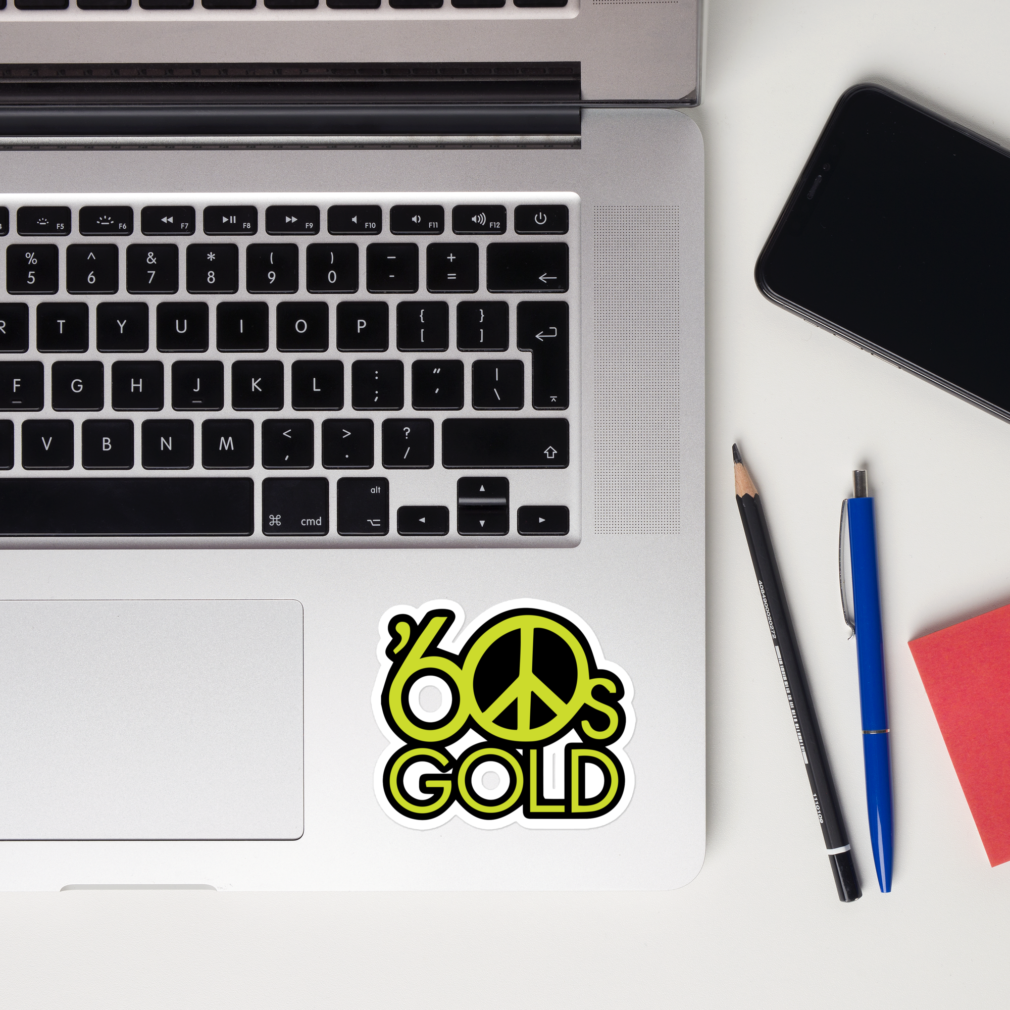 A laptop keyboard displaying a colorful '60s Gold' peace sign sticker.