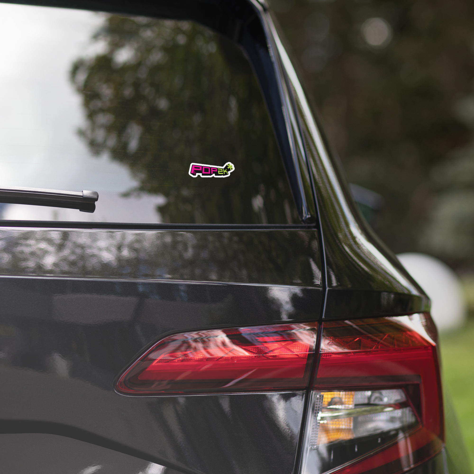 Close-up of a black car's rear with a colorful 'Pop2K' sticker on the back window.