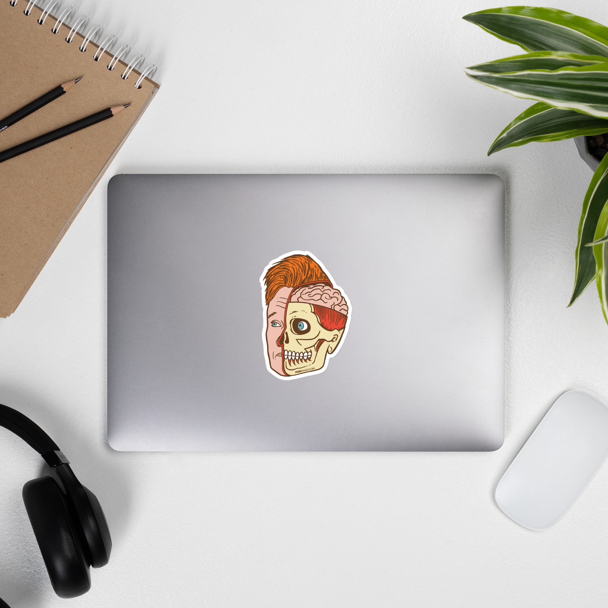 Laptop displaying sticker featuring half of Conan O'Brien's face and half of a skeletal face revealing the brain inside.