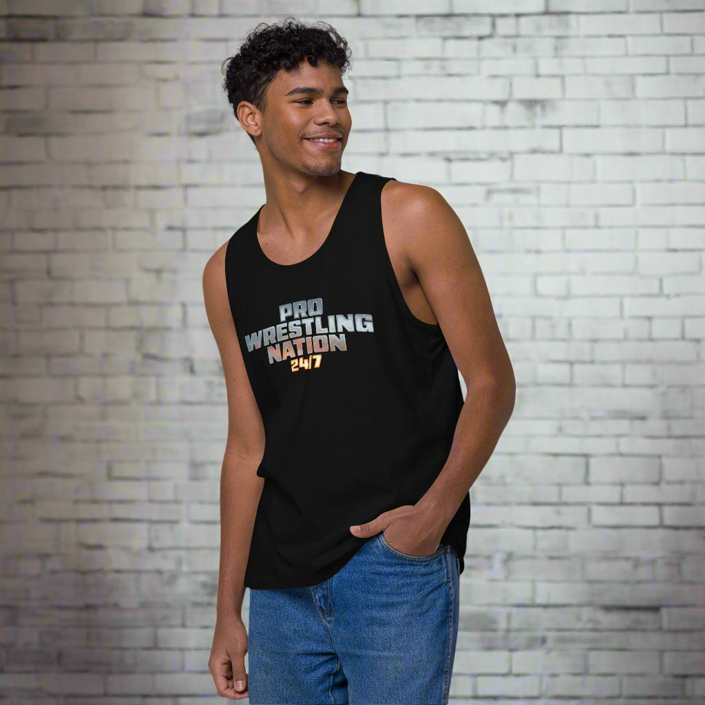 Smiling male model wearing a black 'Pro Wrestling Nation 24/7' tank top, posing in front of a white brick wall.