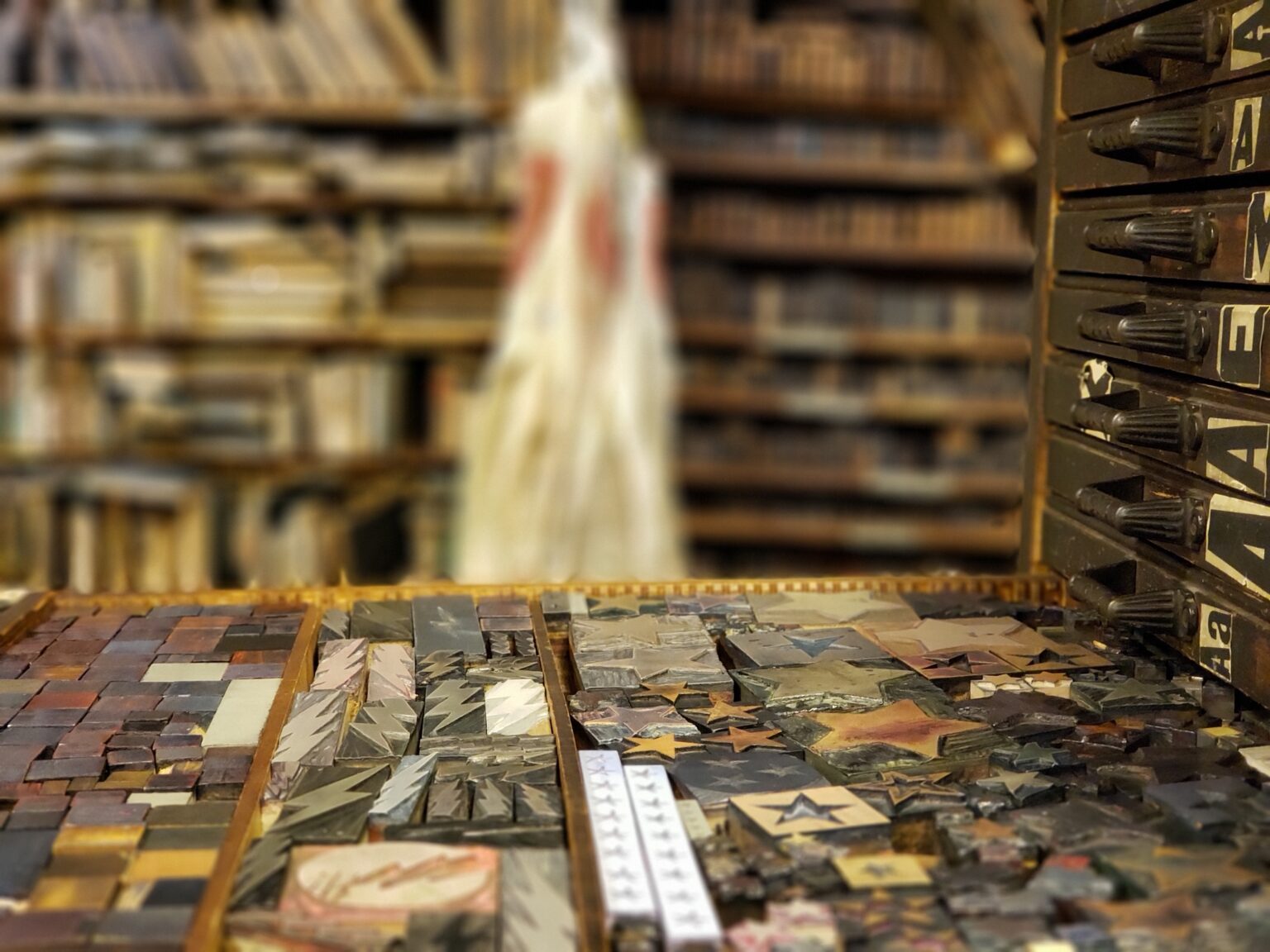 A close-up of wooden printing blocks on a table with shelves of books blurred in the background.