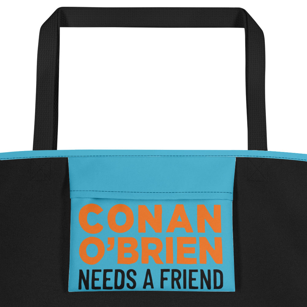Close up of inside pocket of a teal beach bag with black handles, featuring colorful text reading 'CONAN O'BRIEN NEEDS A FRIEND.'