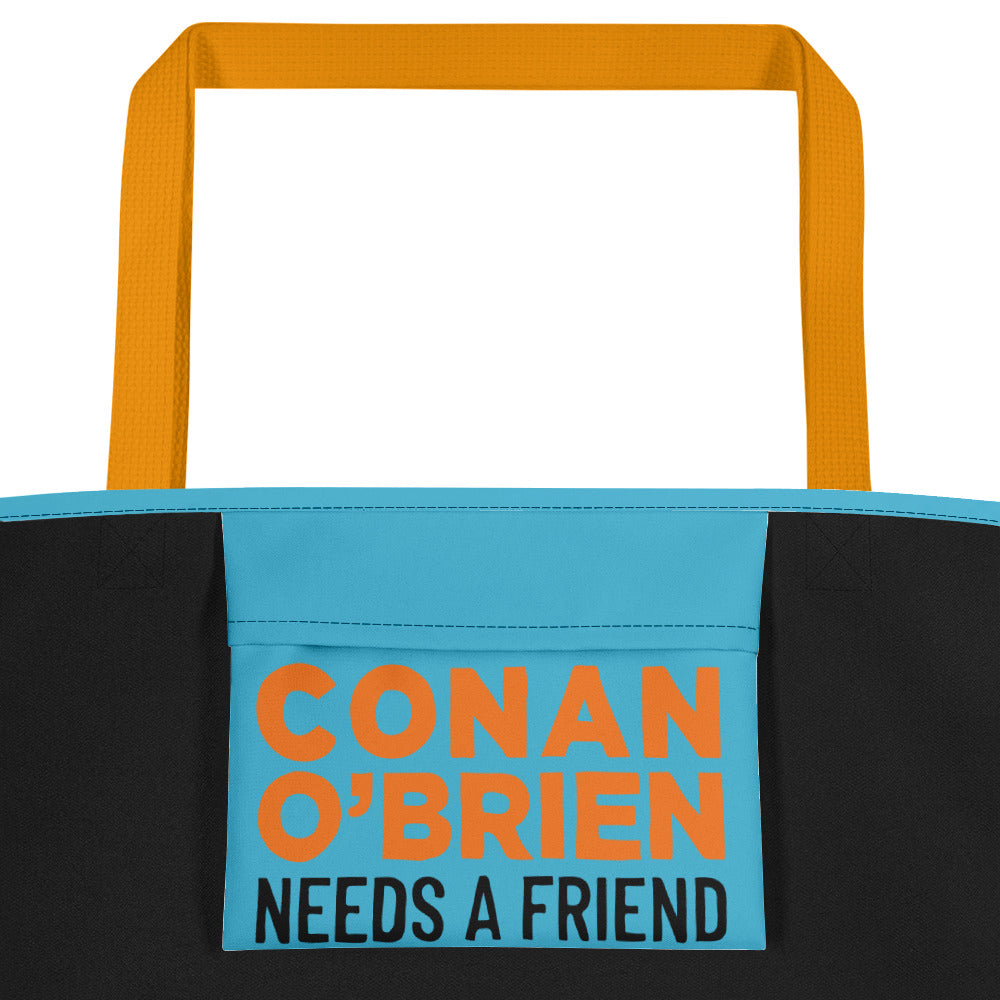 Close up of inside pocket of a teal beach bag with yellow handles, featuring colorful text reading 'CONAN O'BRIEN NEEDS A FRIEND.'