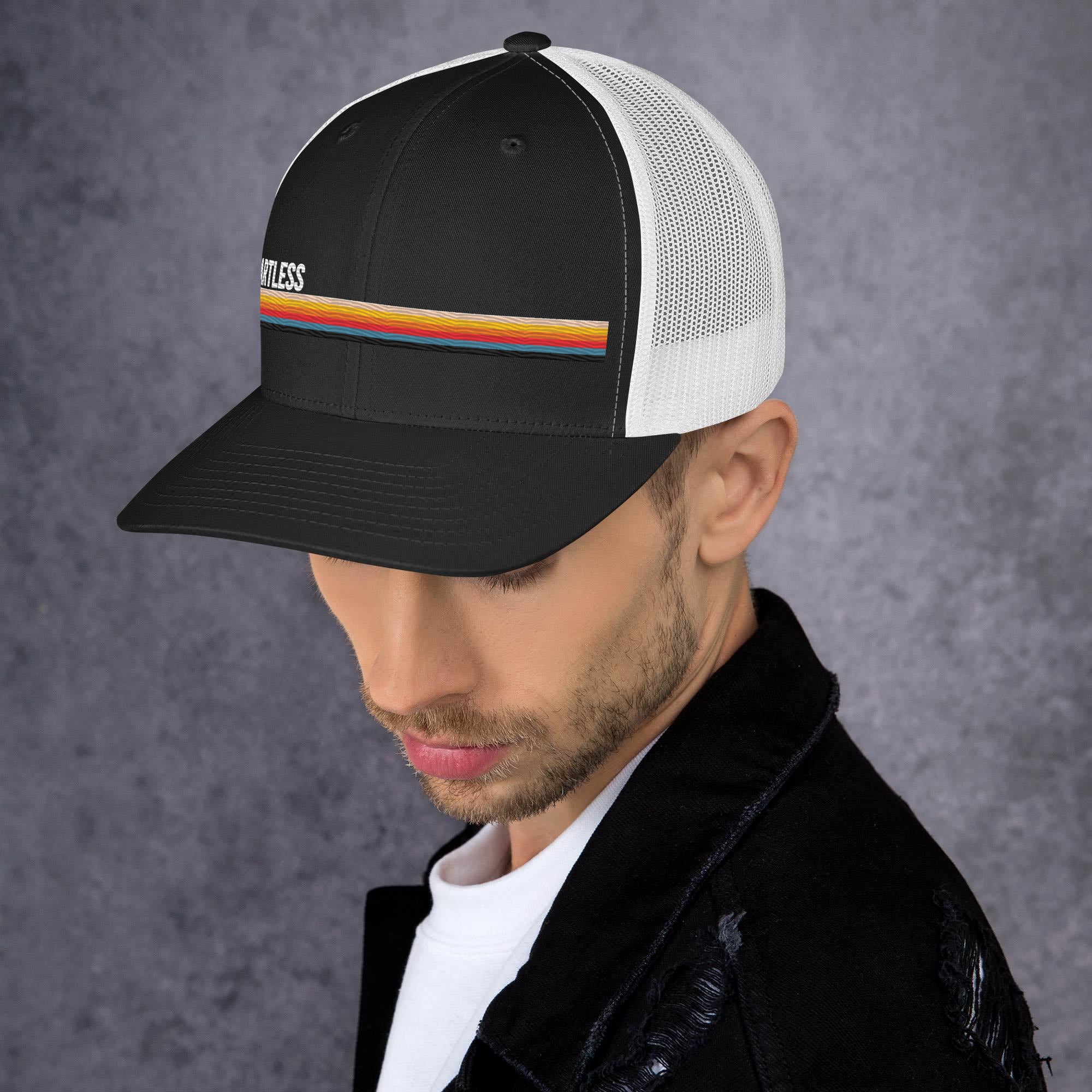Person wearing a black and white trucker hat with a colorful stripe and the word 'SmartLess,' set against a black background.