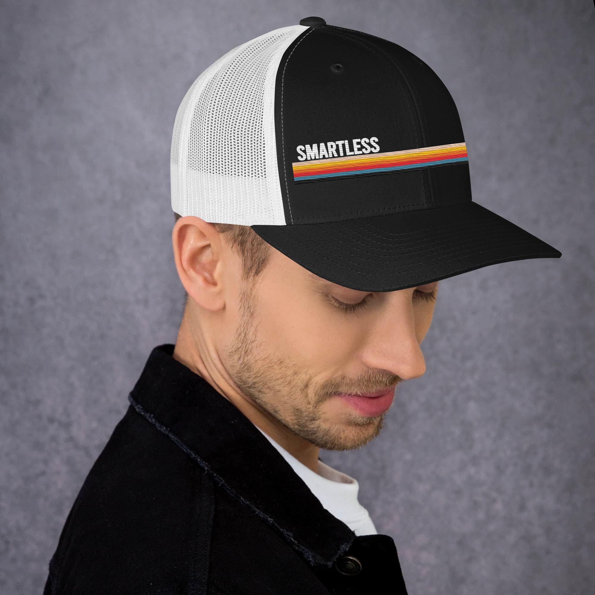 A man wearing a black and white trucker hat with the word 'SMARTLESS' and a colorful stripe on the front.