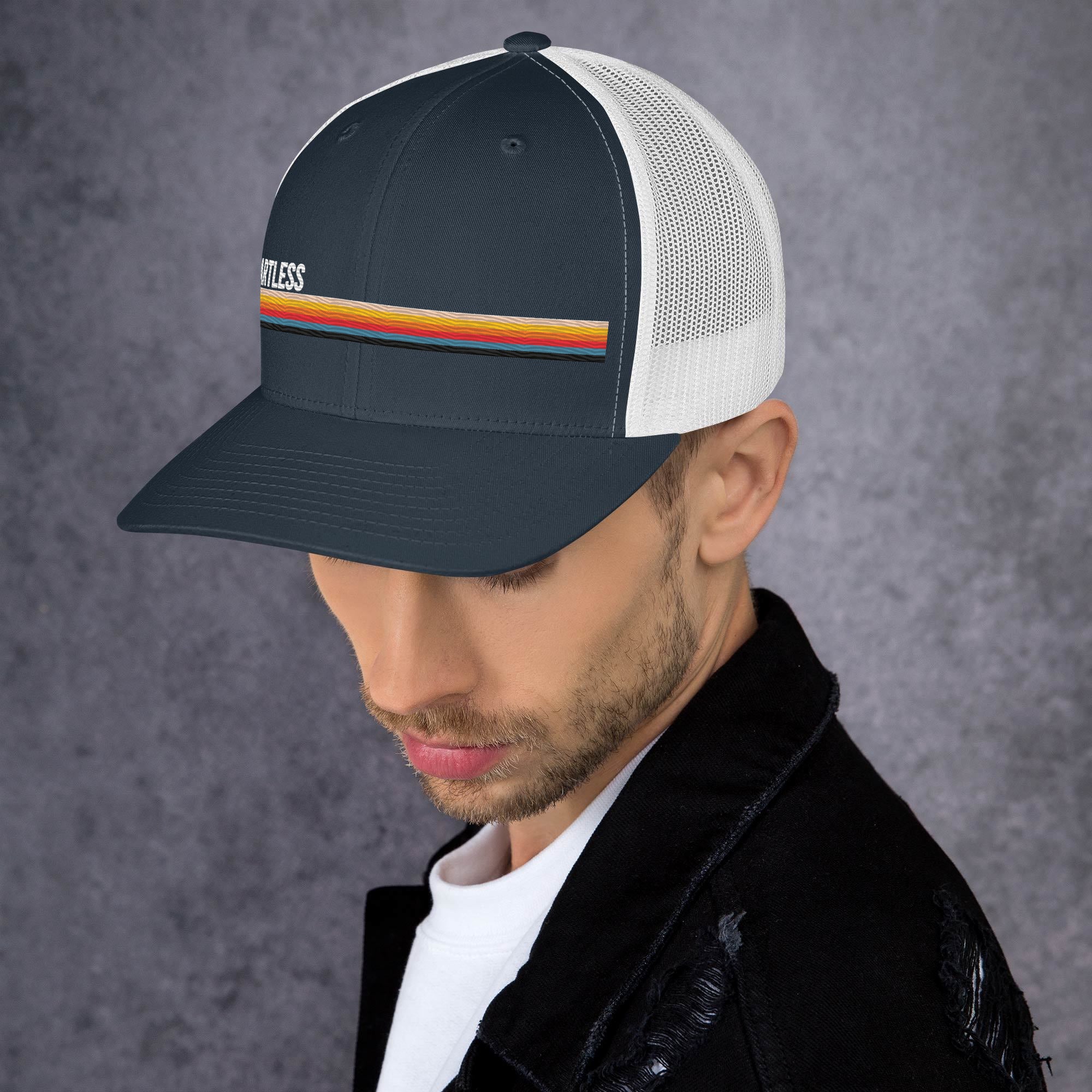 A man wearing a navy blue and white trucker hat with a colorful stripe and the word 'SmartLess' embroidered on the front.