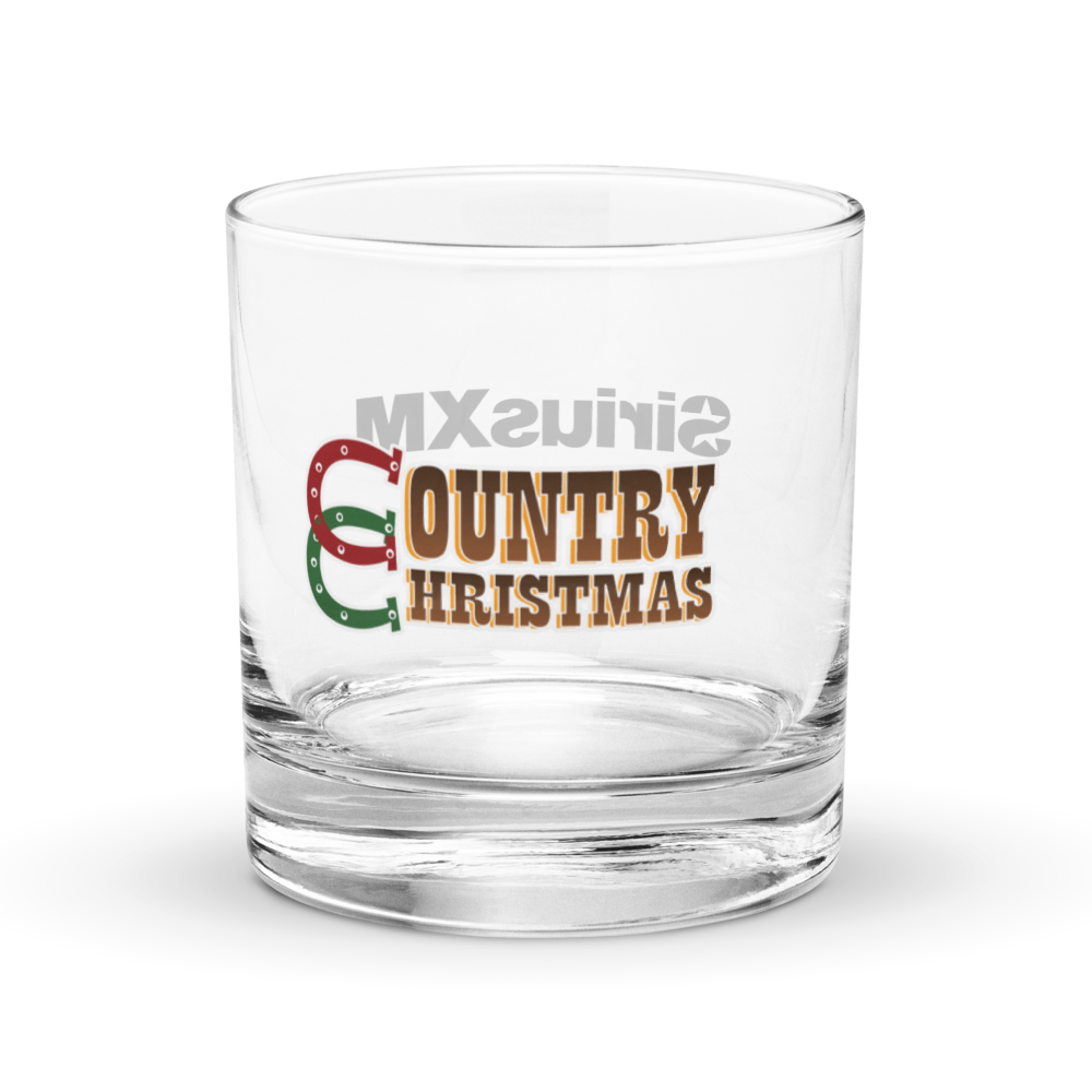 Clear rocks glass featuring the ‘Country Christmas’ logo on the front, with a red, green, and brown horseshoe forming the letter ‘C’; the standalone ‘SiriusXM’ logo printed on the back of the glass is faintly visible through the transparent surface.