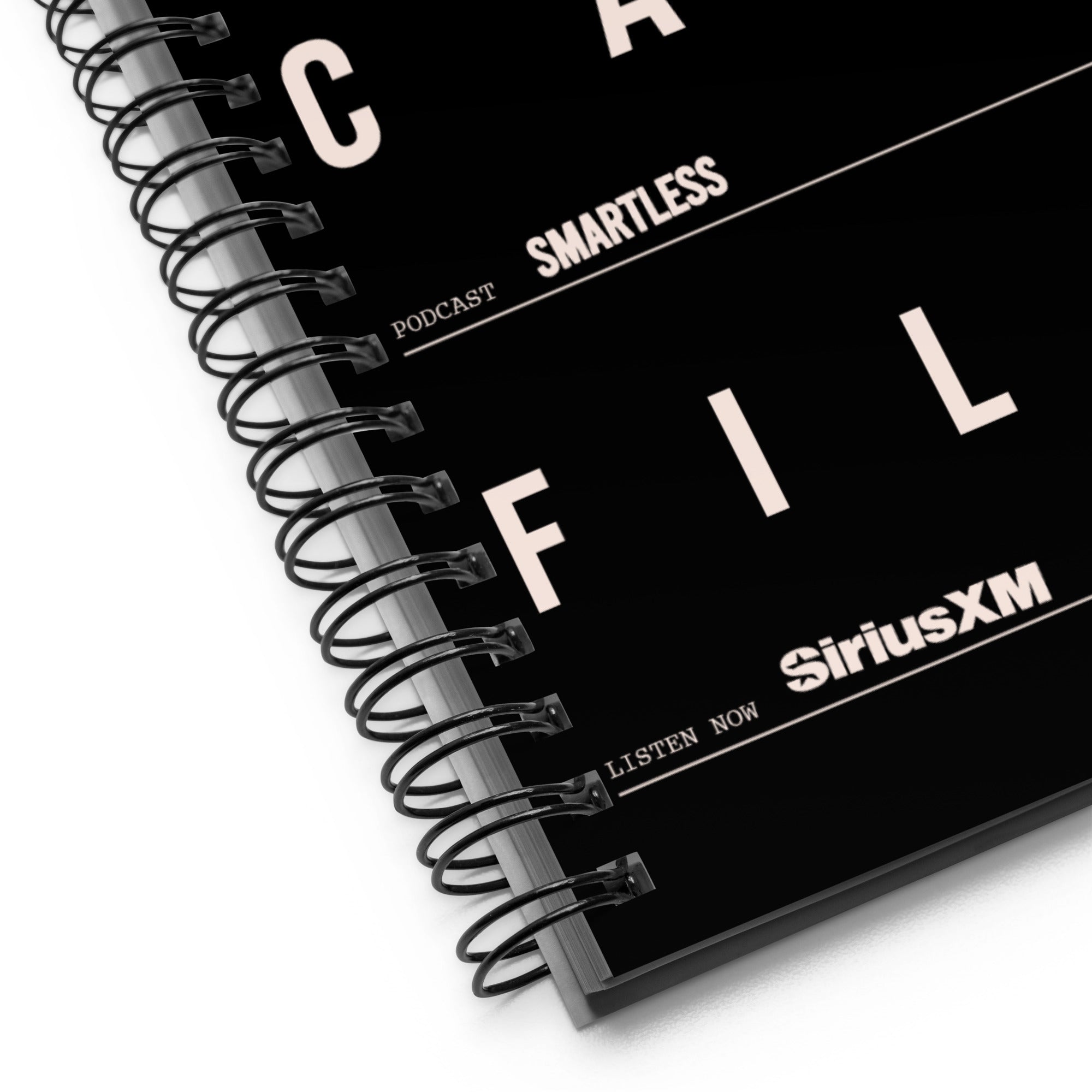 Detailed close-up of the bottom left corner of the black spiral notebook. The black metal coil binding is visible, along with white block letters spelling ‘FILES’, and the white logos ‘SmartLess’ and ‘SiriusXM’ in smaller print.