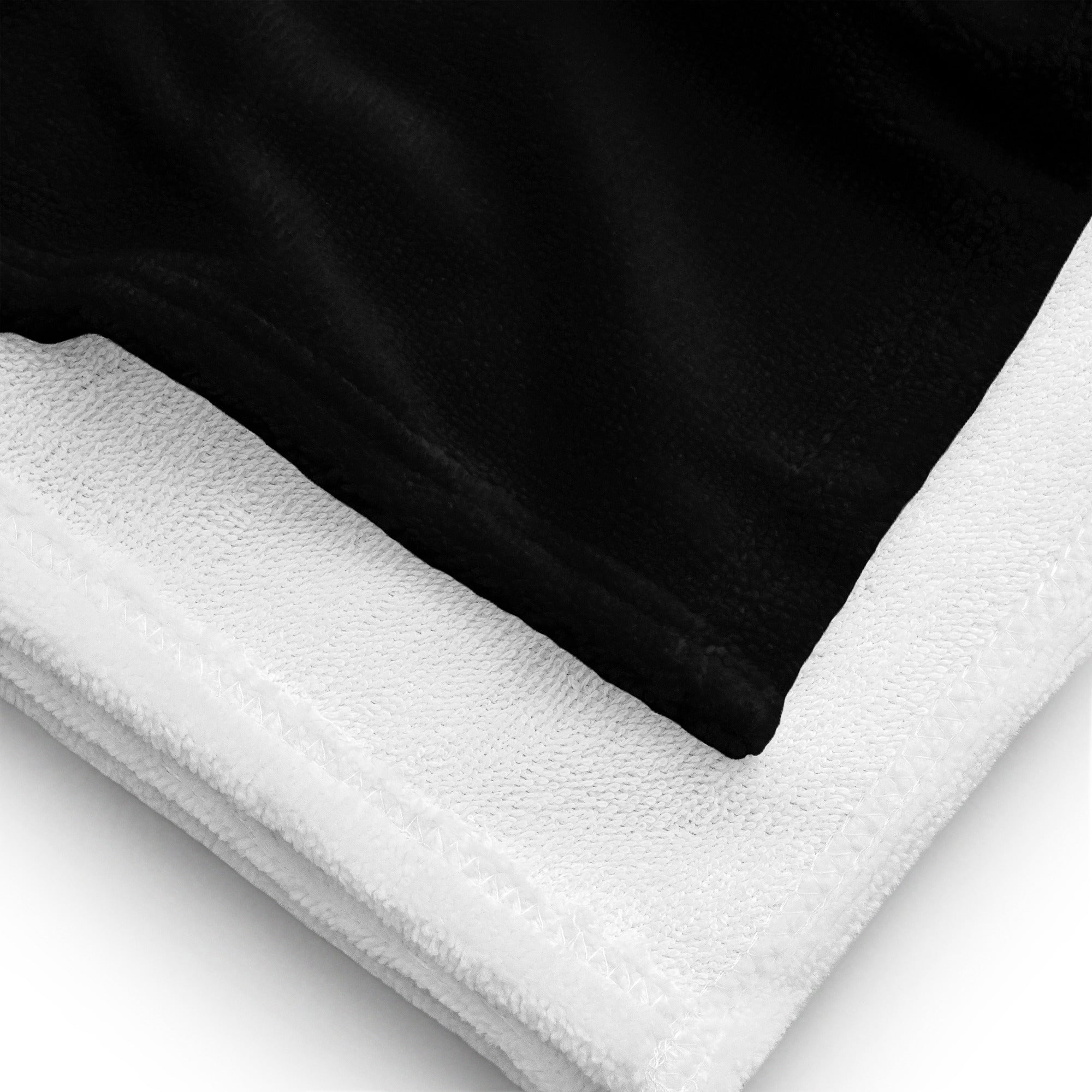 A close-up of a folded black towel with a soft white underside, showing the stitching detail and plush texture of the fabric.