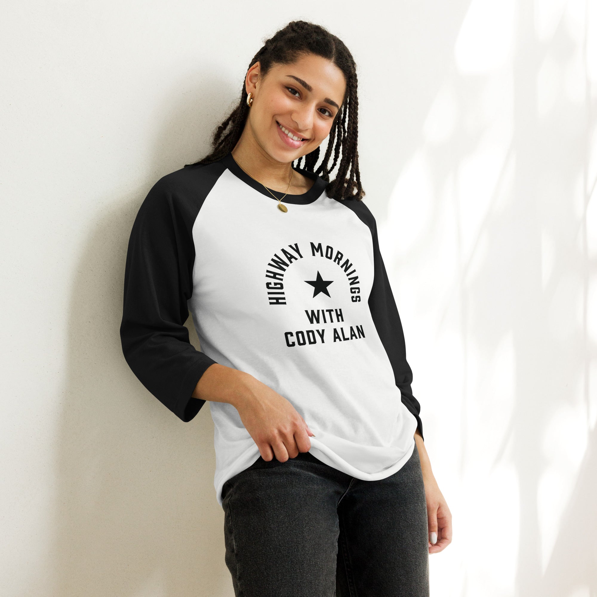 A smiling woman wearing a black and white raglan shirt featuring the 'HIGHWAY MORNINGS WITH CODY ALAN' text and star design in black across the front.