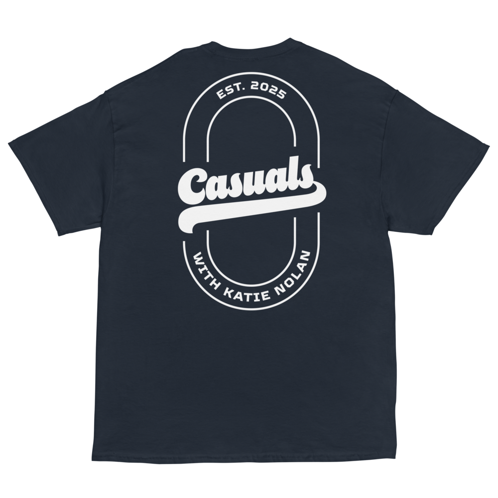 Navy short-sleeve t-shirt laid flat, featuring a large white oval outline on the back with bold text 'Casuals' in the center, 'EST. 2025' above, and curved text 'WITH KATIE NOLAN' below.