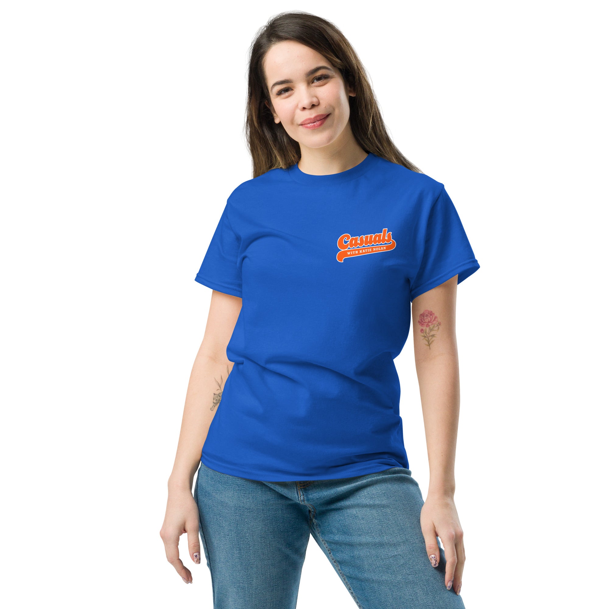 A woman smiling while wearing a royal blue short-sleeve T-shirt with a small orange and white front logo that reads 'Casuals WITH KATIE NOLAN' in retro-style lettering.