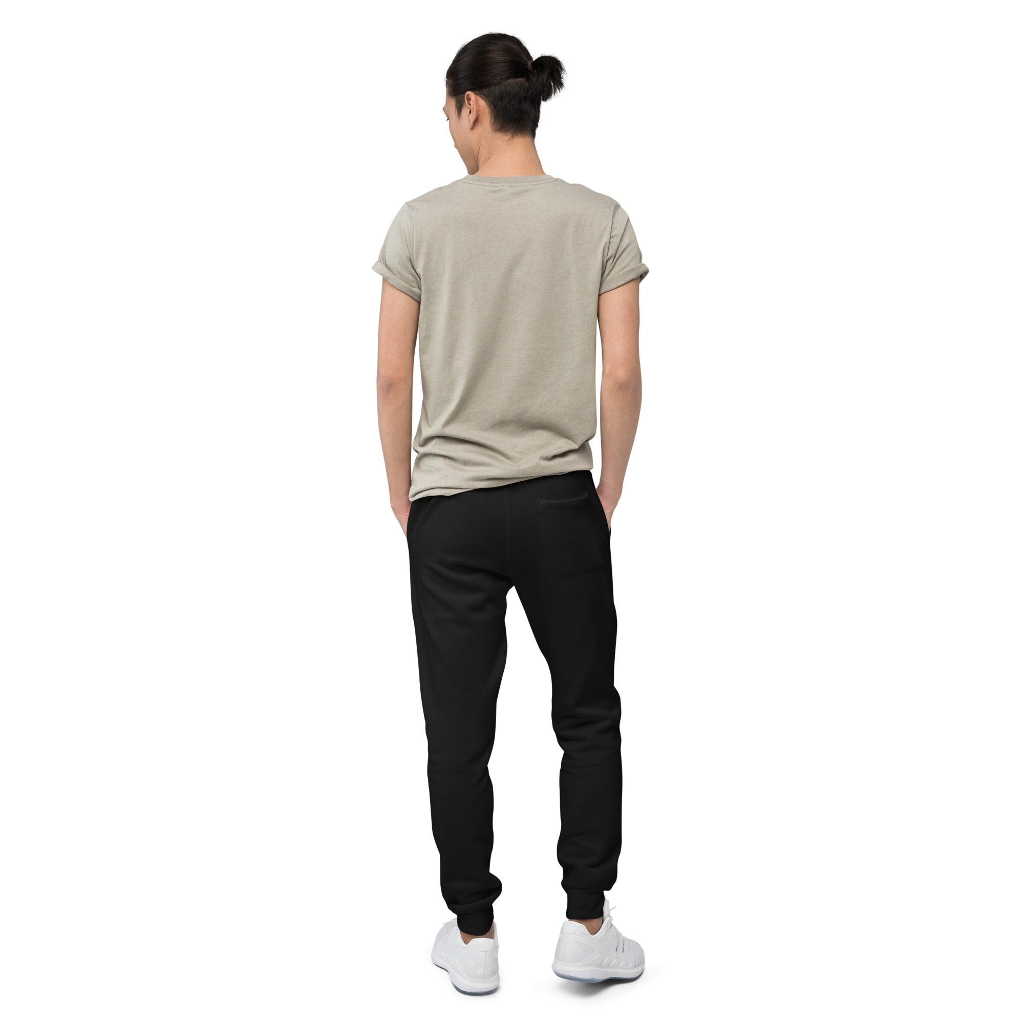Back view of a person wearing black sweatpants with a plain design and a visible back pocket, paired with a light beige t-shirt and white sneakers.