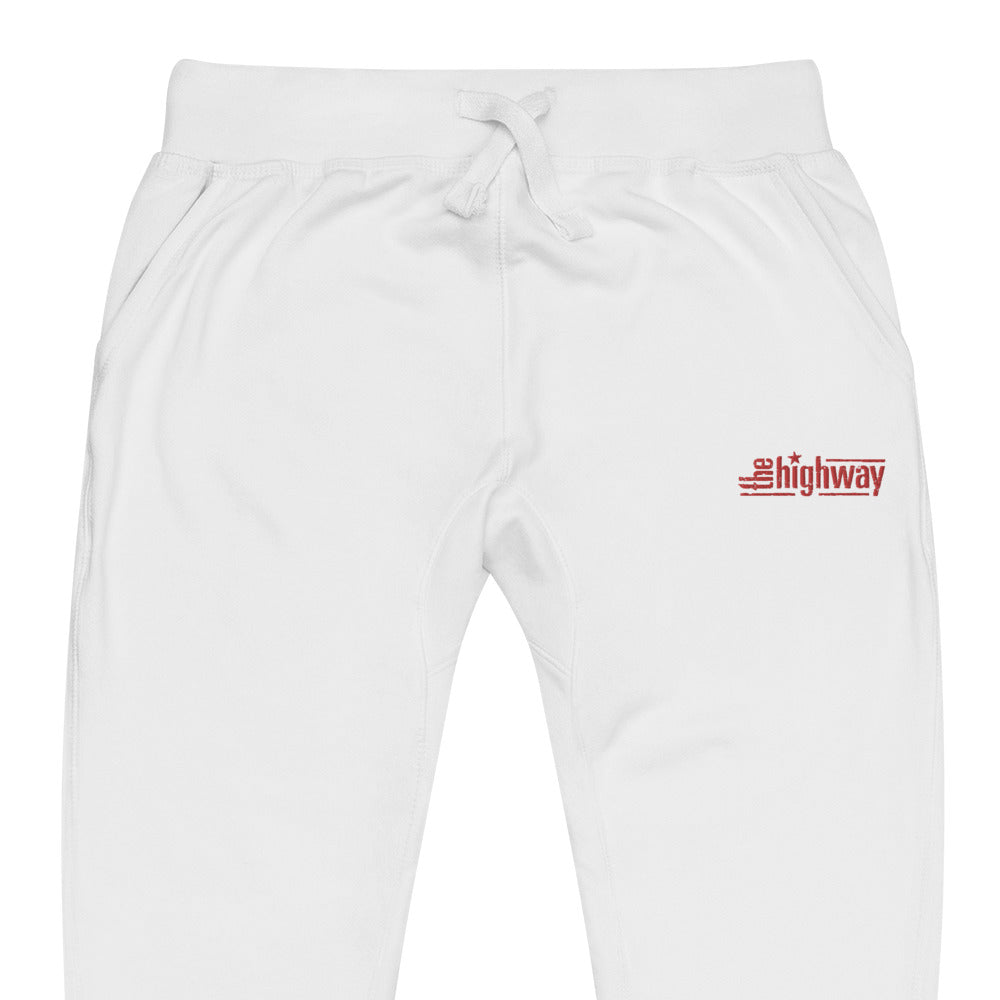 Close up of white sweatpants with a red 'the highway' logo on the left thigh and side pockets.