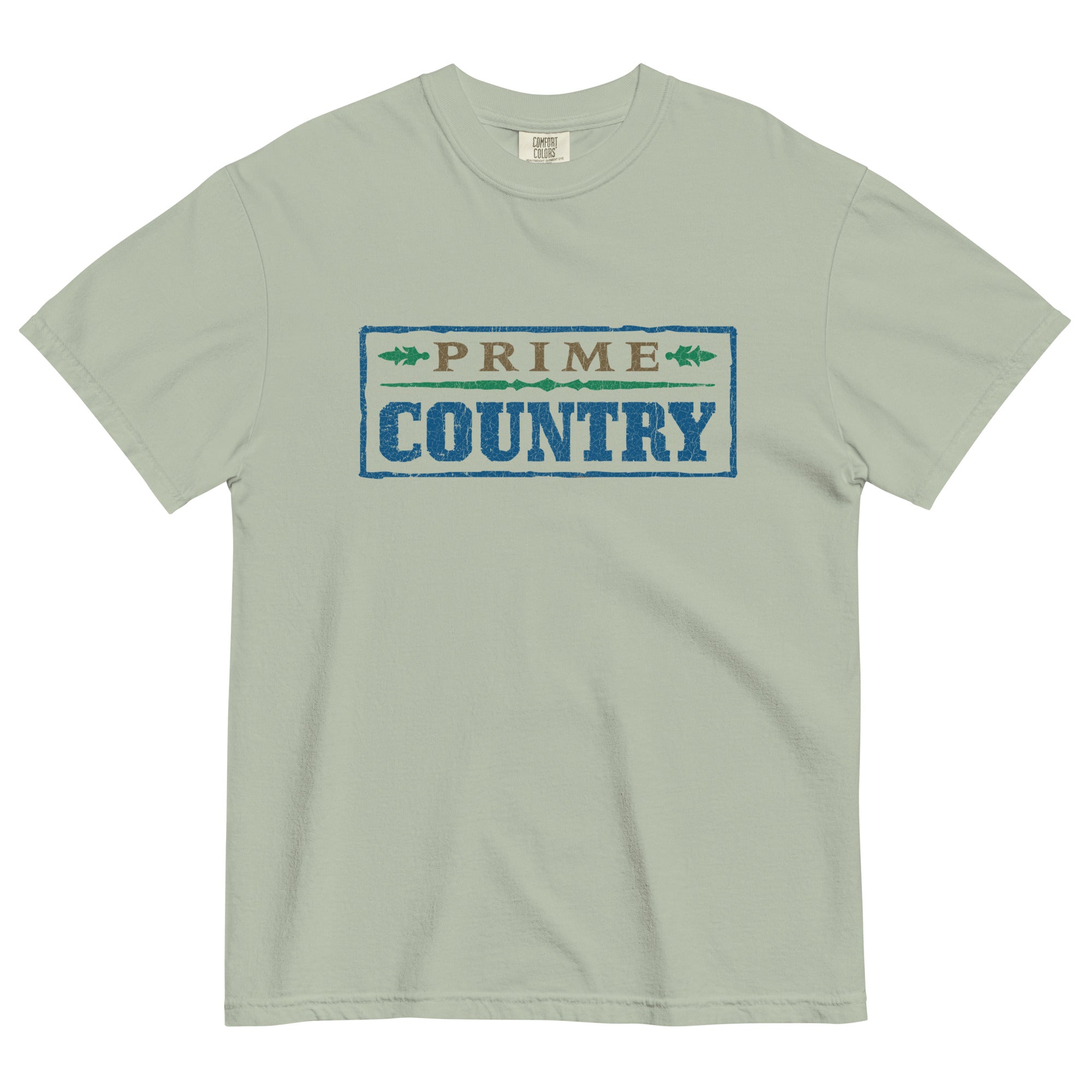 Flat lay of a sage green T-shirt with the same front design as above. The shirt displays the large distressed 'PRIME COUNTRY' logo, with 'PRIME' in brown and 'COUNTRY' in bold blue, separated by green arrowhead accents and framed in a textured rectangular border.