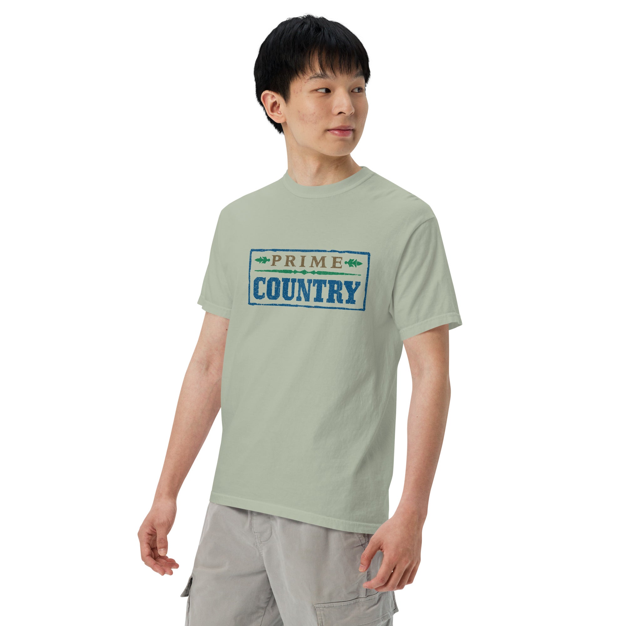 A man faces forward wearing the T-shirt. The front 'PRIME COUNTRY' print is clearly shown, highlighting the rustic typography and vintage-style color palette of brown, blue, and green.