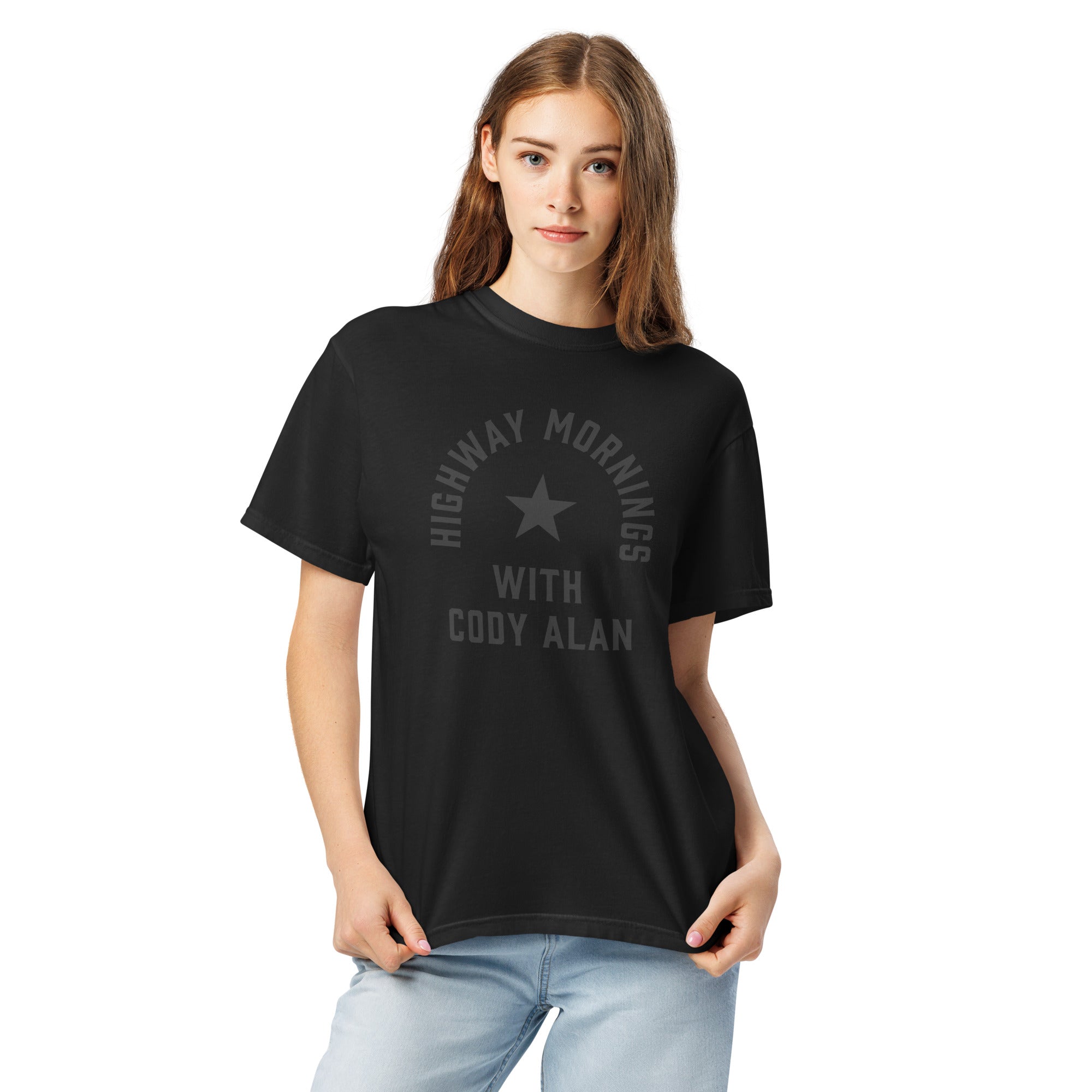A woman shown from the front wearing a black short-sleeve T-shirt with light blue jeans. The shirt’s front features a subtle black-on-black design with a star in the center and the text 'HIGHWAY MORNINGS WITH CODY ALAN' printed in black above and below the star.