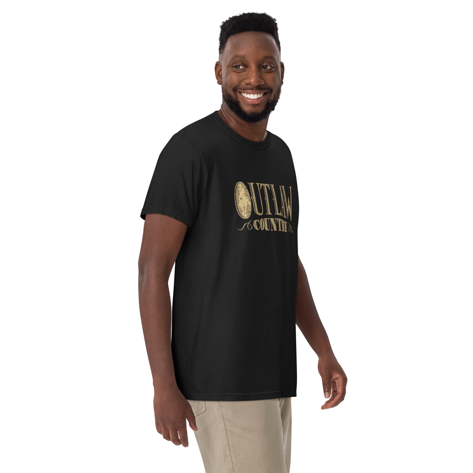 Man facing slightly left wearing the black T-shirt. The front graphic reads 'OUTLAW COUNTRY' in distressed gold western-style text, with a vintage oval emblem containing a cowboy silhouette replacing the 'O' in 'OUTLAW'.