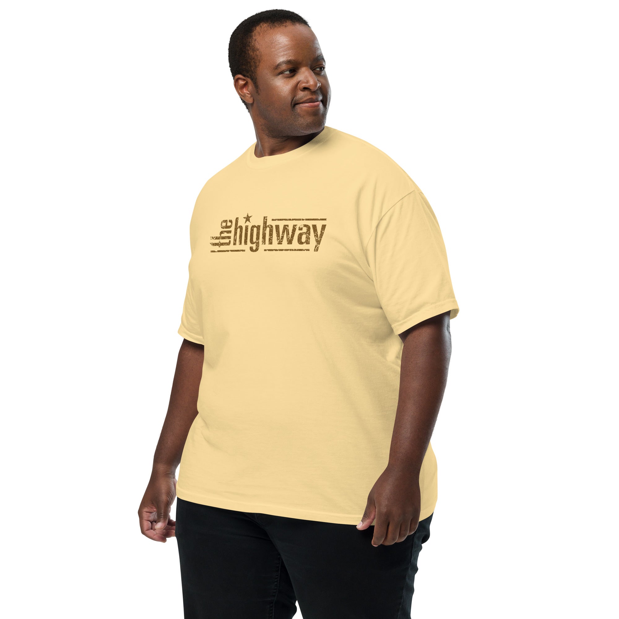 Man wearing a pale yellow T-shirt with the ‘the highway’ logo in distressed brown text across the chest, with a star dotting the i in ‘highway’.