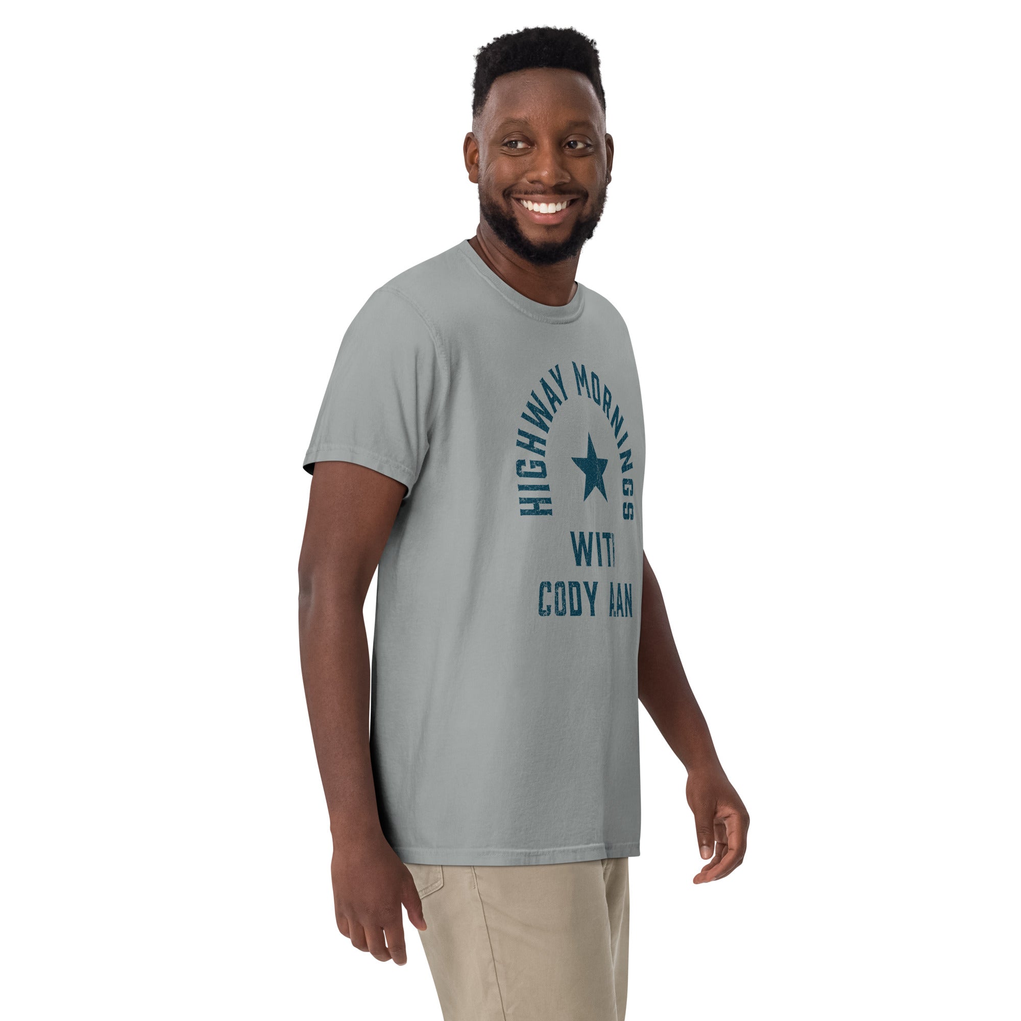 Man smiling and wearing a gray short-sleeve t-shirt with the words 'HIGHWAY MORNINGS WITH CODY ALAN' in a distressed blue font, arranged in an arc around a blue star on the chest.