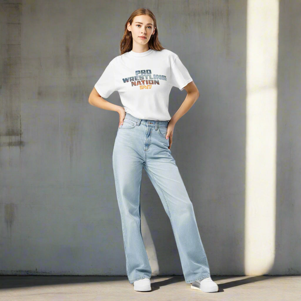Full-body front view of a female model wearing a white 'Pro Wrestling Nation 24/7' T-shirt tucked into light-wash jeans.