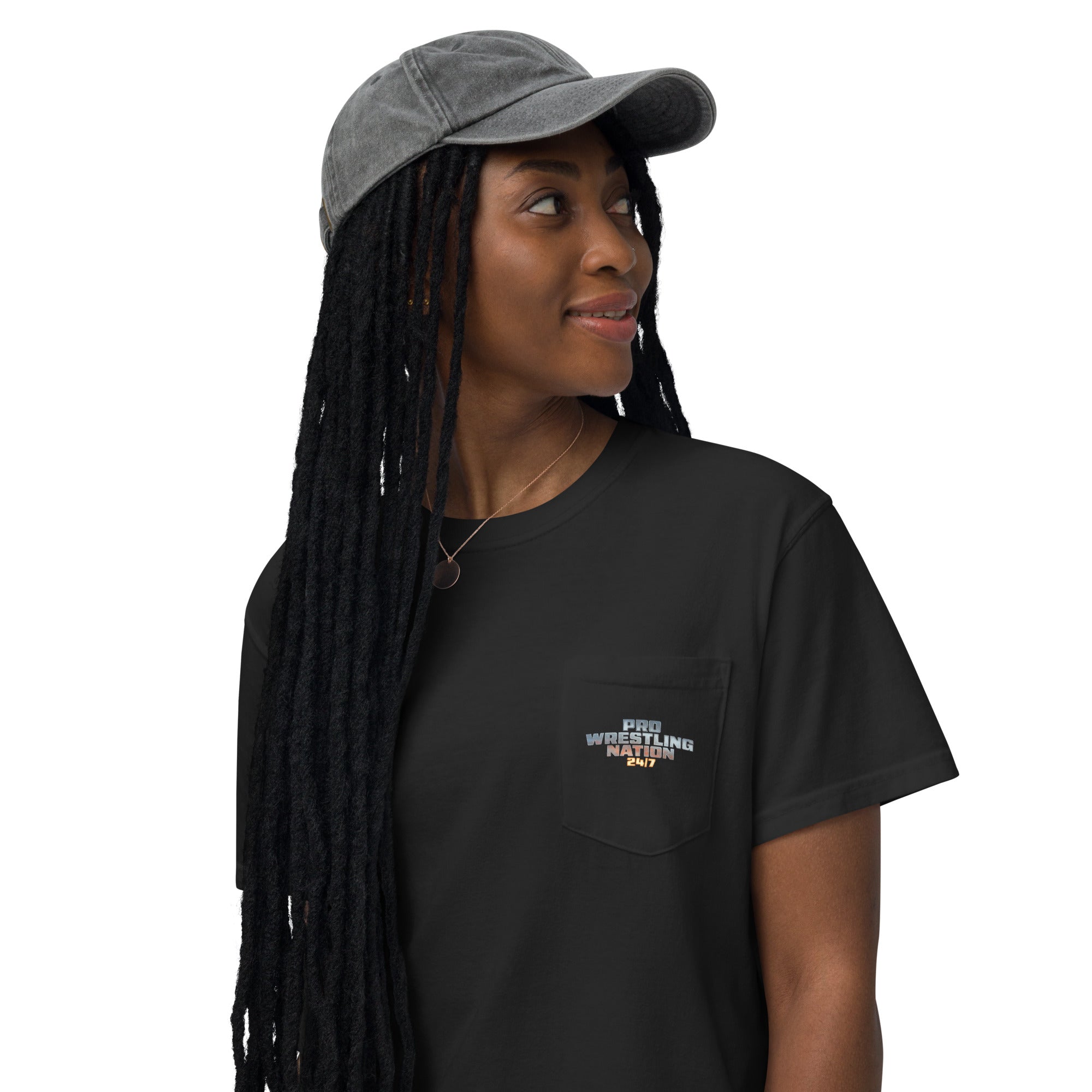 Close-up front view of a woman wearing the black pocket t-shirt, featuring the 'Pro Wrestling Nation 24/7' logo on the front pocket, looking off to the side in a grey cap.