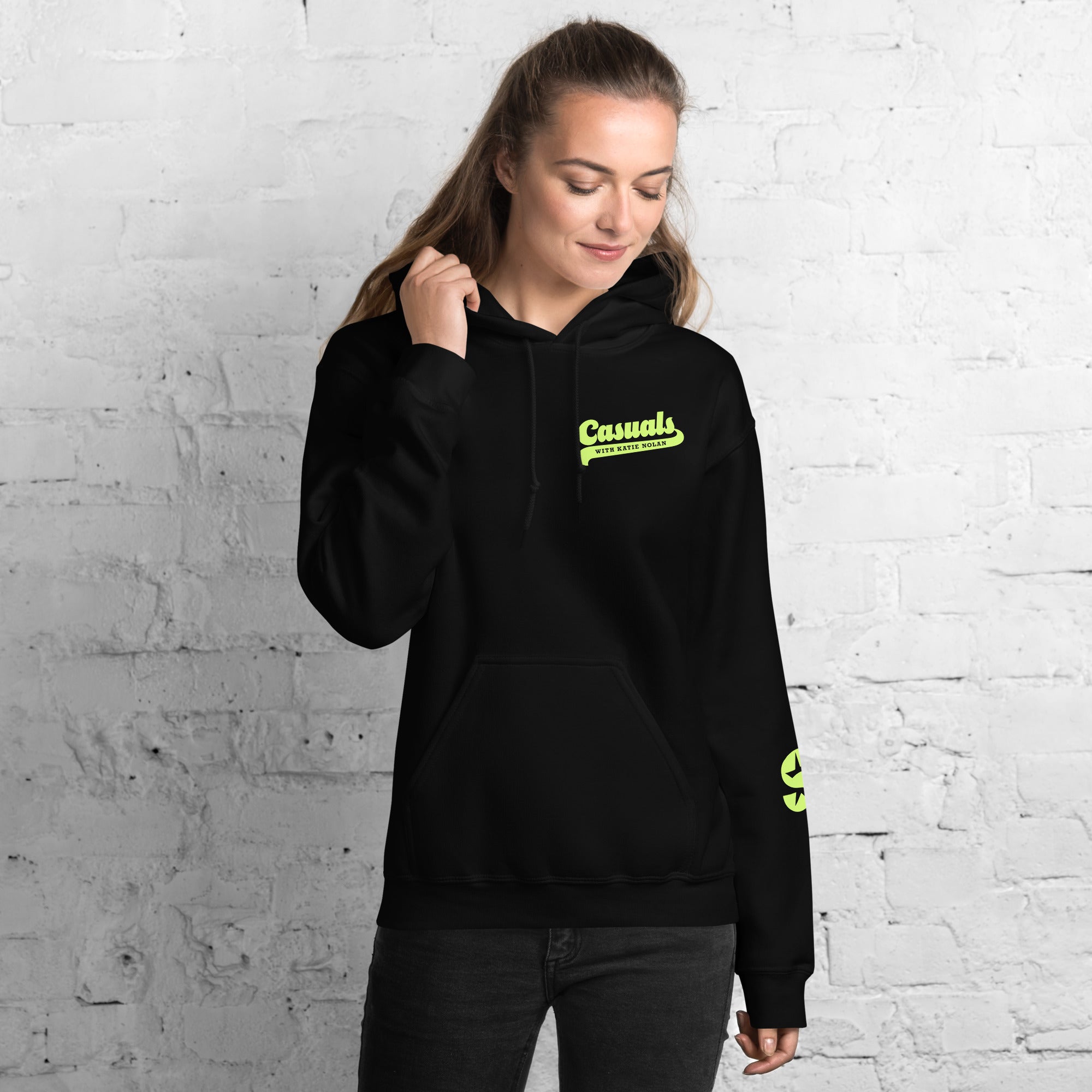 A woman wearing the black hoodie with the 'Casuals with Katie Nolan' text on the left chest in light green; SiriusXM’s 'S-Star' logo is also visible on the right sleeve.