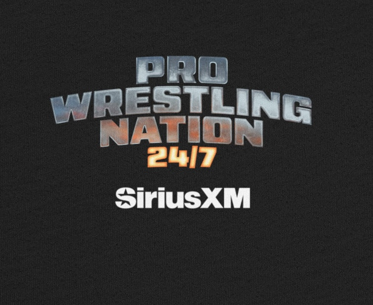 Flat lay of a black T-shirt showing the full back design featuring the metallic text 'PRO WRESTLING NATION 24/7' and white 'SiriusXM' logo centered at the upper back.